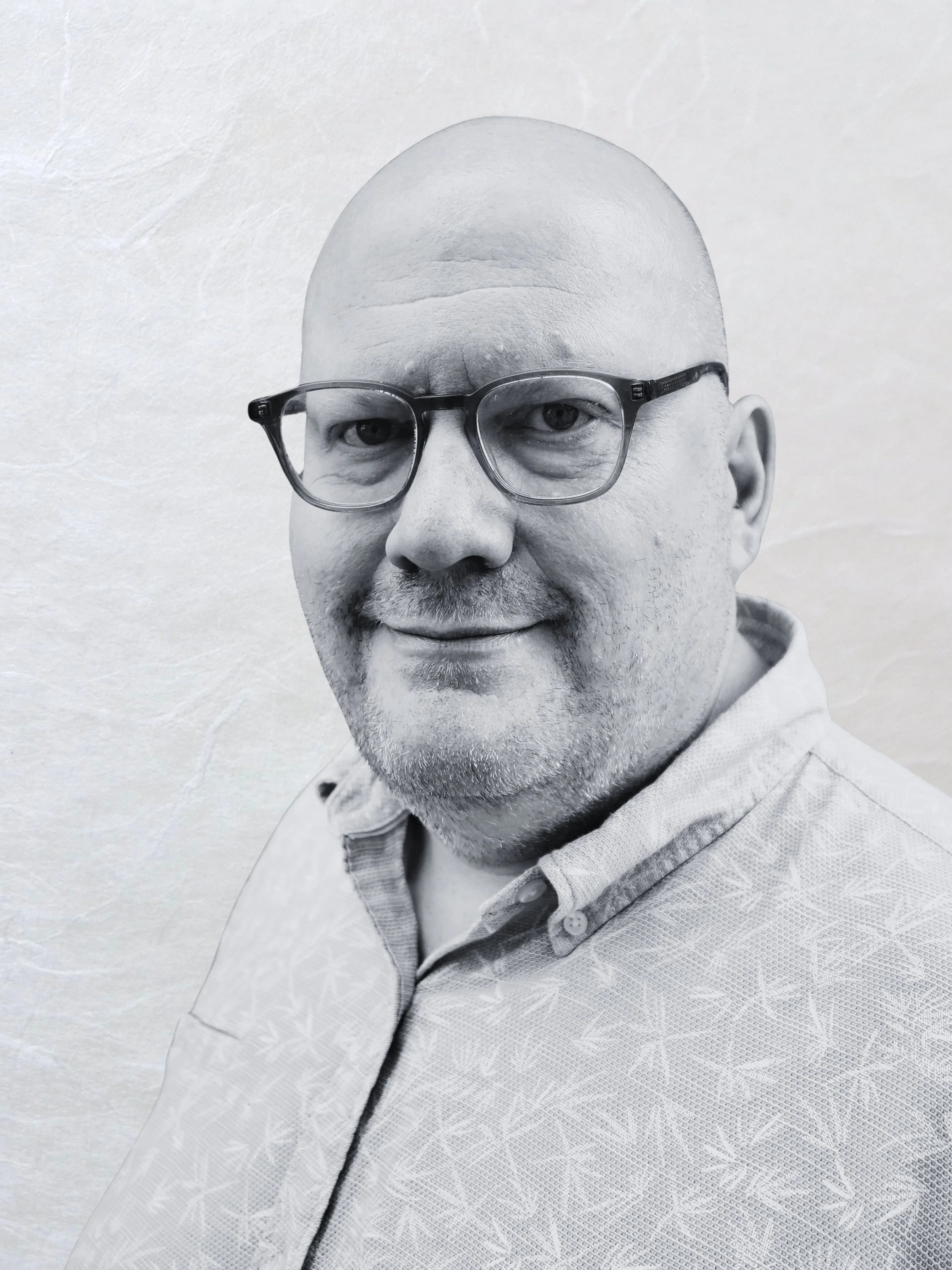 Black and white portrait of a middle-aged man wearing glasses and a collared shirt, smiling slightly, with a textured background.