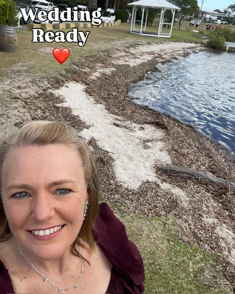 A smiling woman taking a selfie outdoors near a lake, with a white gazebo and a walking path in the background; overlay text reads "Wedding Ready" with a red heart emoji.