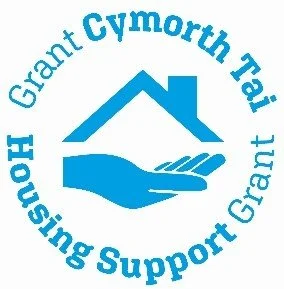 Logo of Grant Cymorth Trai Housing Support Grant, featuring a blue house above an open hand, with the organization name in a circular arrangement.