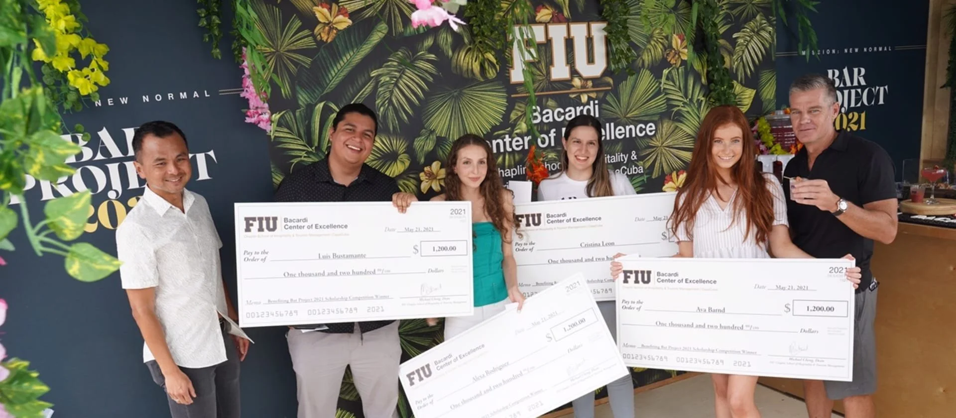 A group of people posing with checks in front of a tropical background.