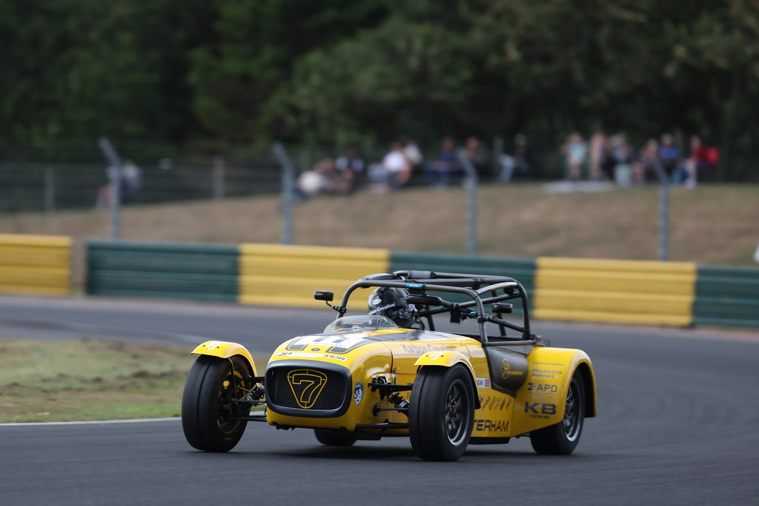 A yellow race car on a track with spectators in the background.