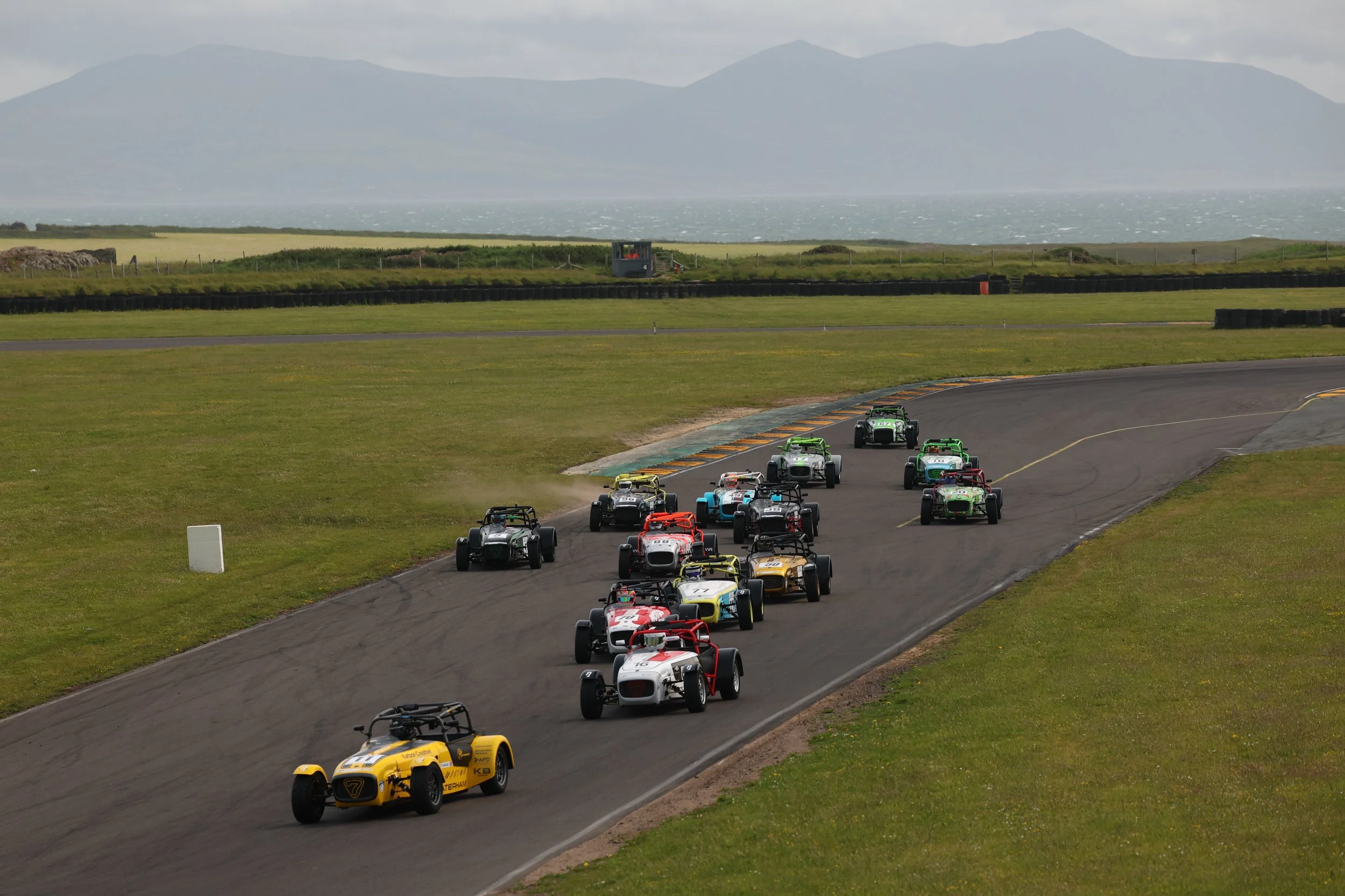 A group of race cars on a race track near a body of water with mountains in the background.