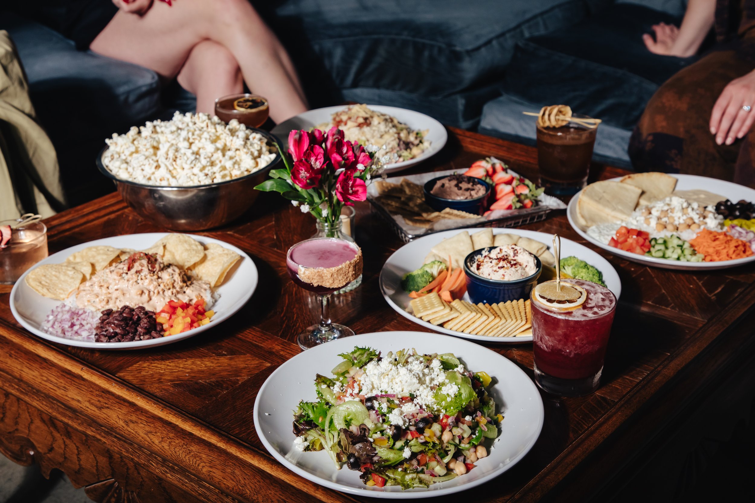 A table filled with various dishes and drinks, including salads, dips, strawberries, and cocktails.