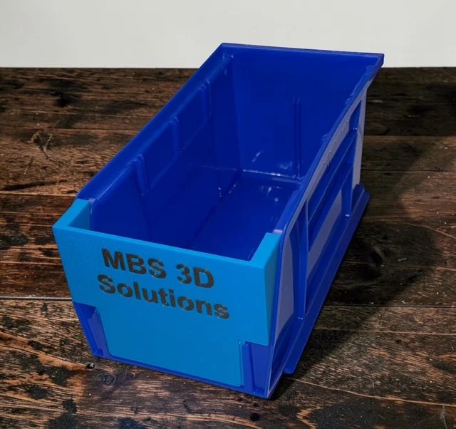 A blue Dillon ammo bin with a bin insert for the RL1050 and RL1100 presses resting on a brown surface.