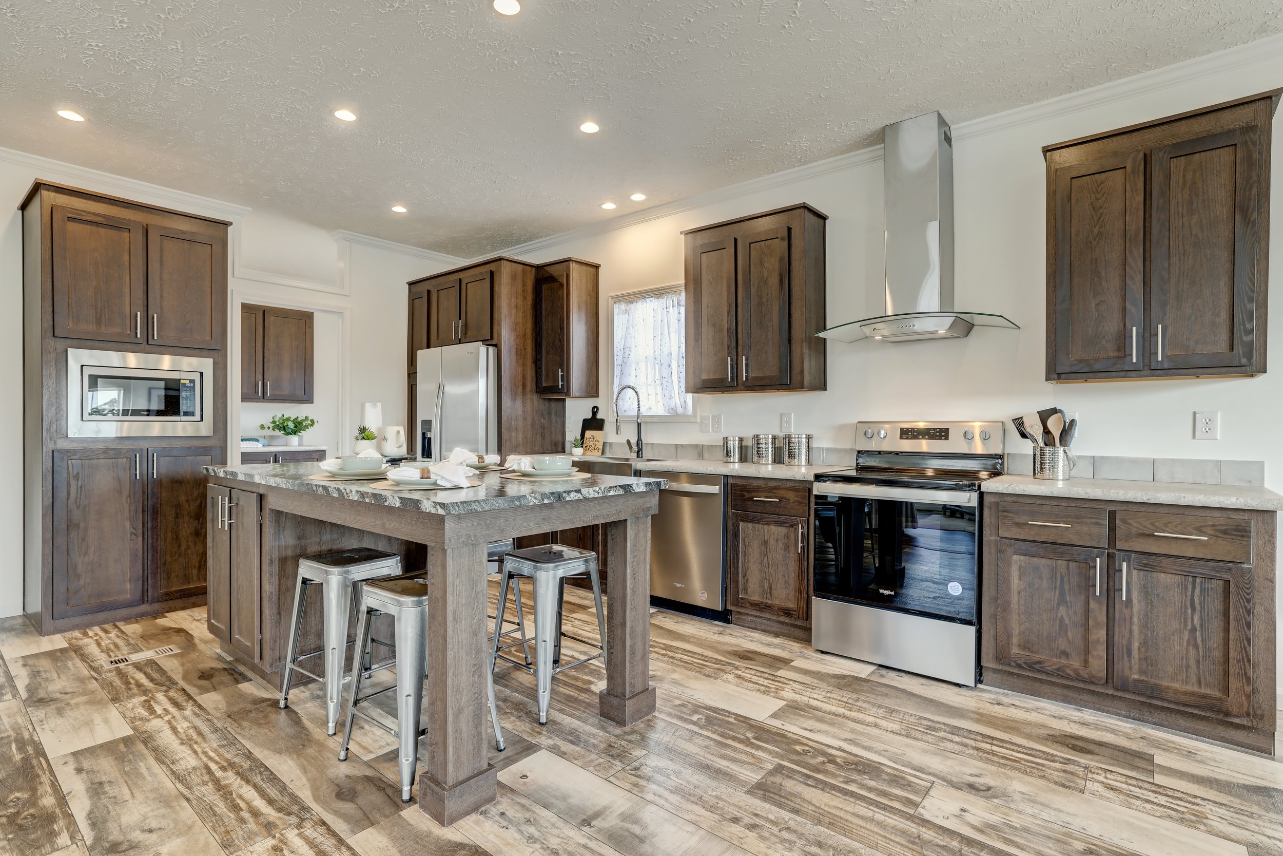 Modern kitchen with wooden cabinets, stainless steel appliances, and island with bar stools and place settings.