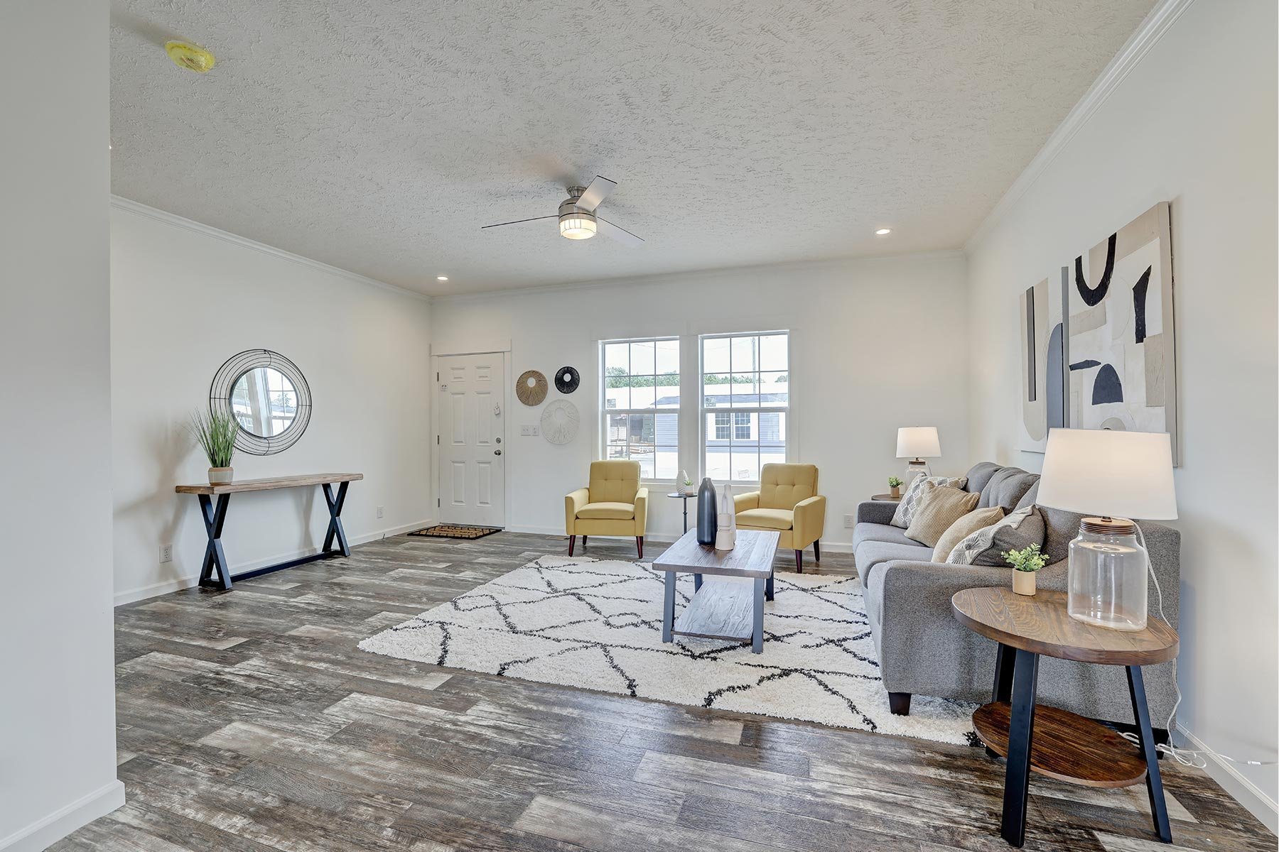 Modern living room with gray couch, two yellow chairs, wooden coffee table, and decorative elements. Features hardwood flooring, a large area rug, and wall art.