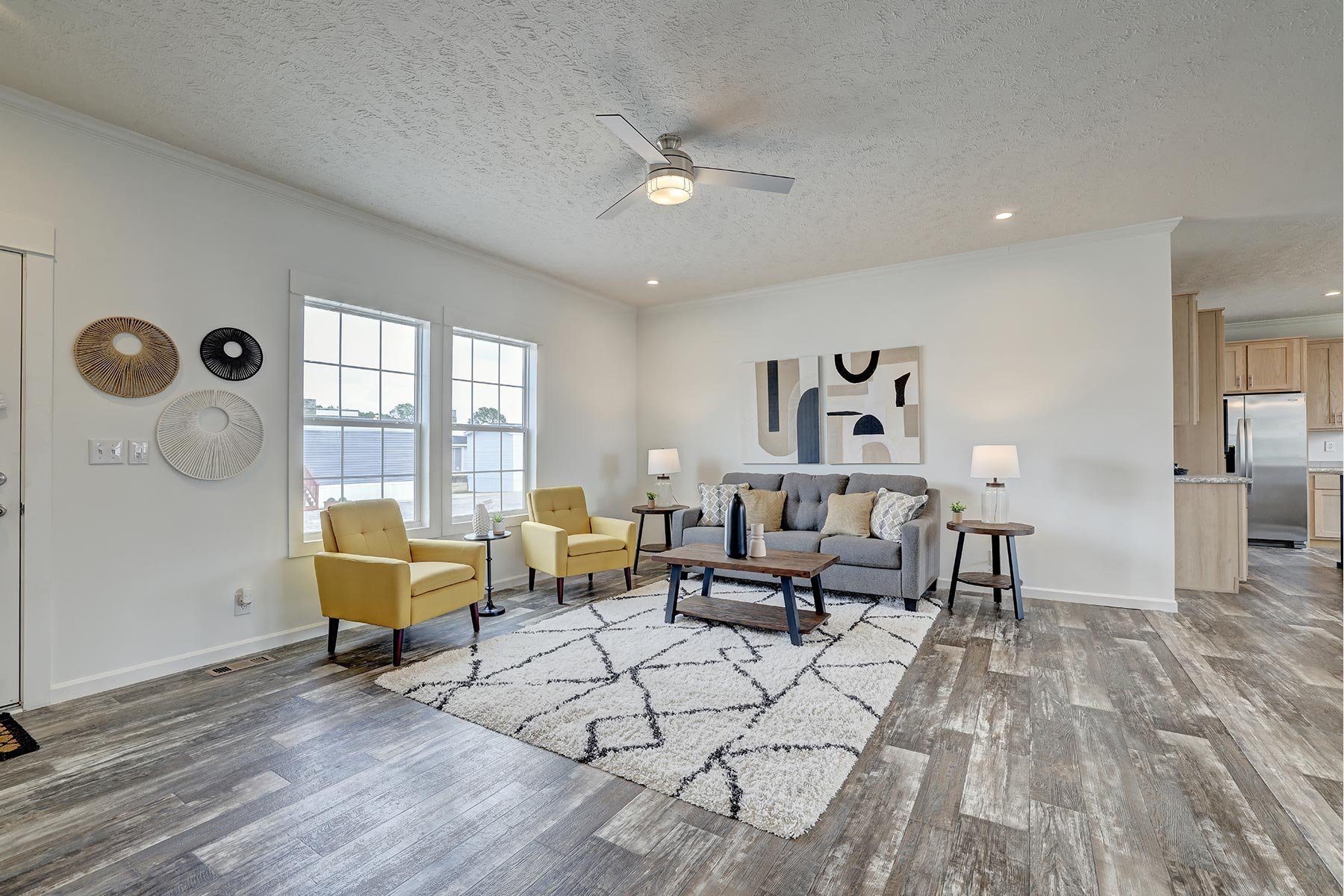 Modern living room with yellow chairs, gray sofa, abstract wall art, wood flooring, and a ceiling fan.