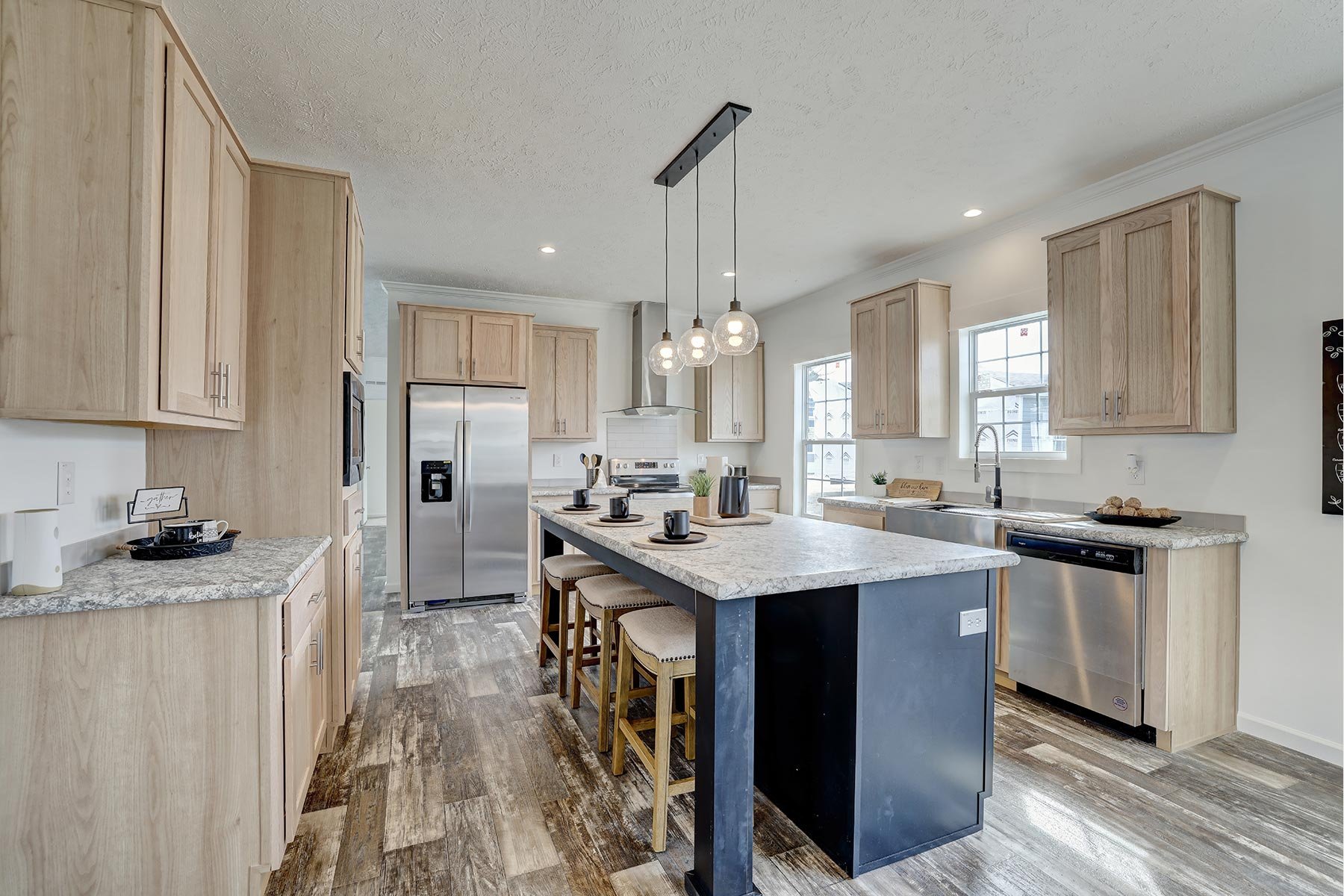 Modern kitchen with wood cabinets, granite countertops, stainless steel appliances, and an island with seating and pendant lighting.