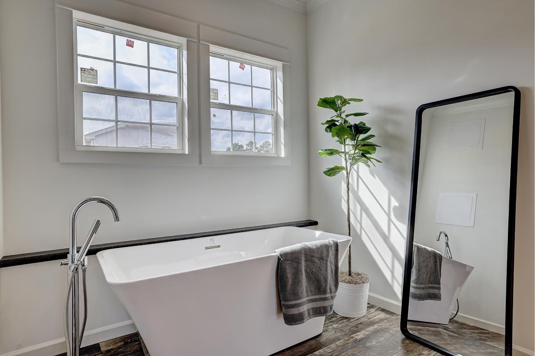 Modern bathroom with a freestanding bathtub, a floor mirror, a potted plant, and two windows.