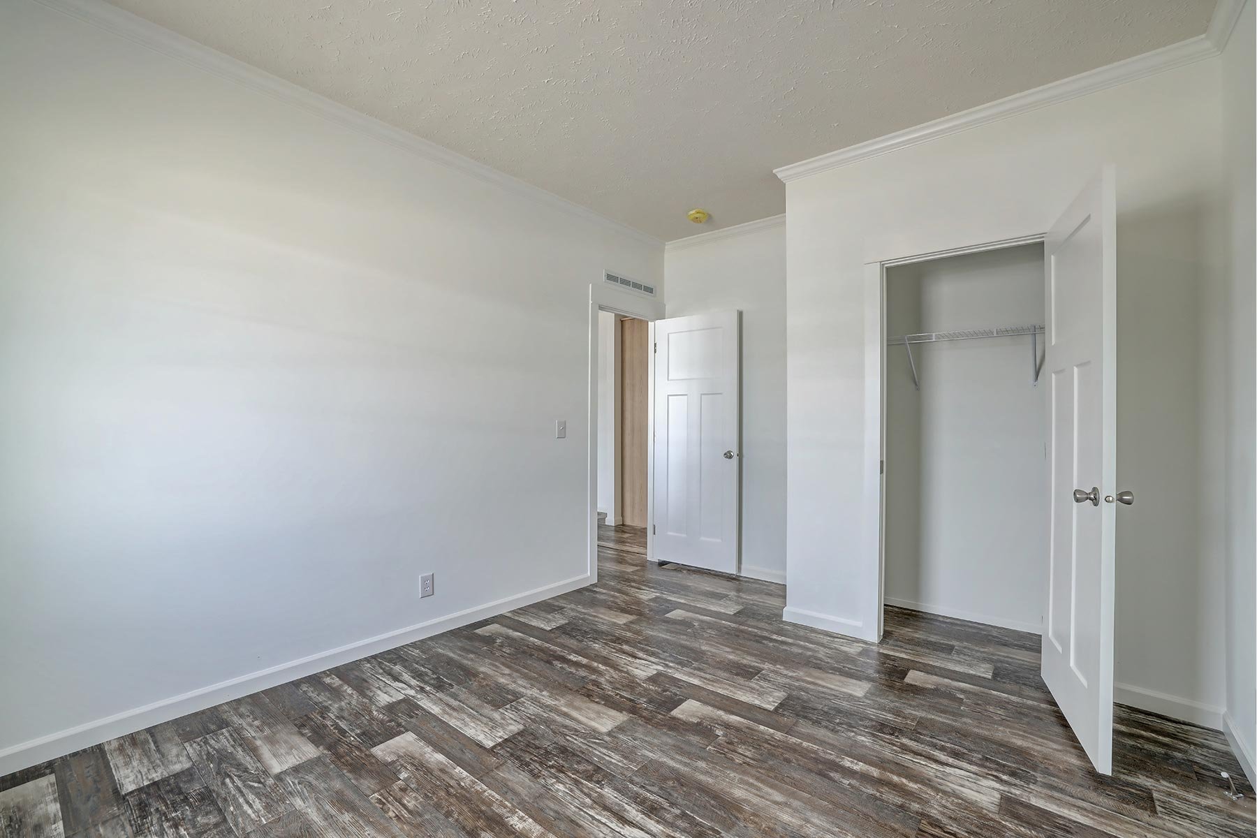 Empty room with wood flooring, white walls, and an open closet door.
