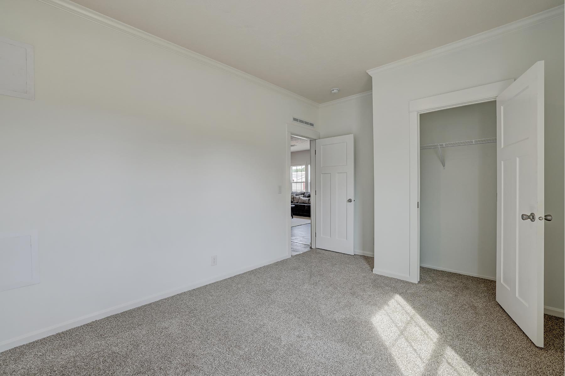 Empty room with beige carpet and open closet, featuring partly open door to adjacent room with sunlight streaming in.