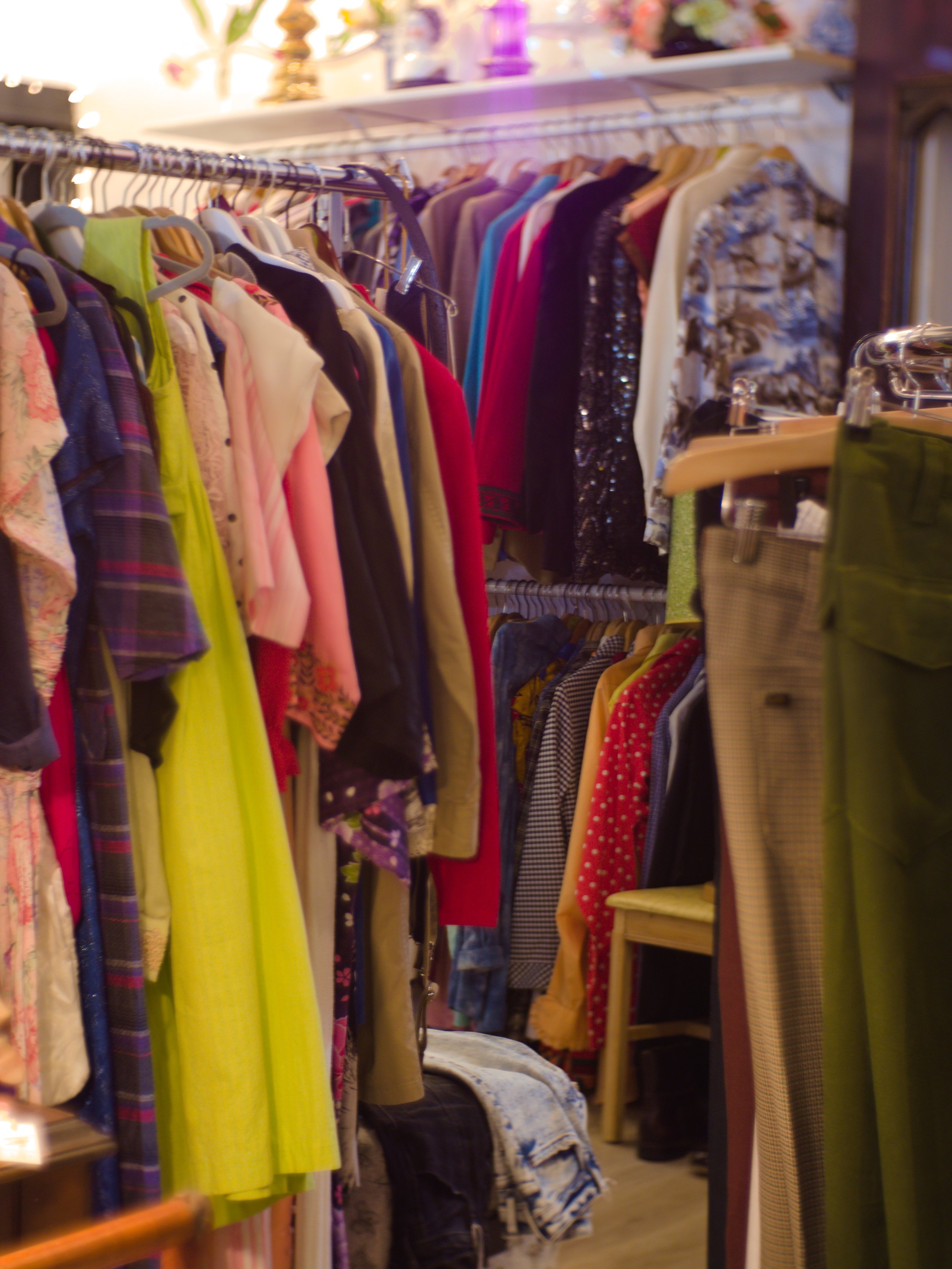 Clothes hanging on racks in a vintage clothing store. Various garments including dresses, shirts, and jackets in different colors and patterns.