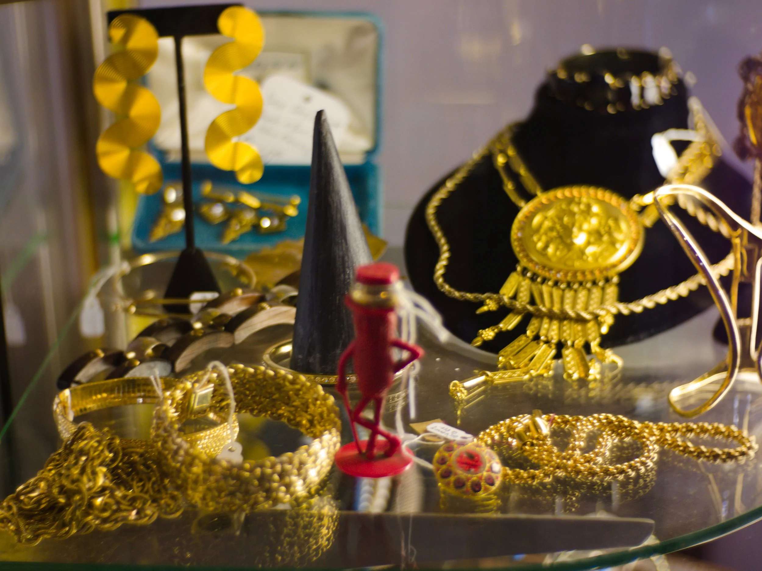 Display case with gold jewelry including chains, bracelets, and earrings, along with decorative items like a yellow pinwheel and small figurines.