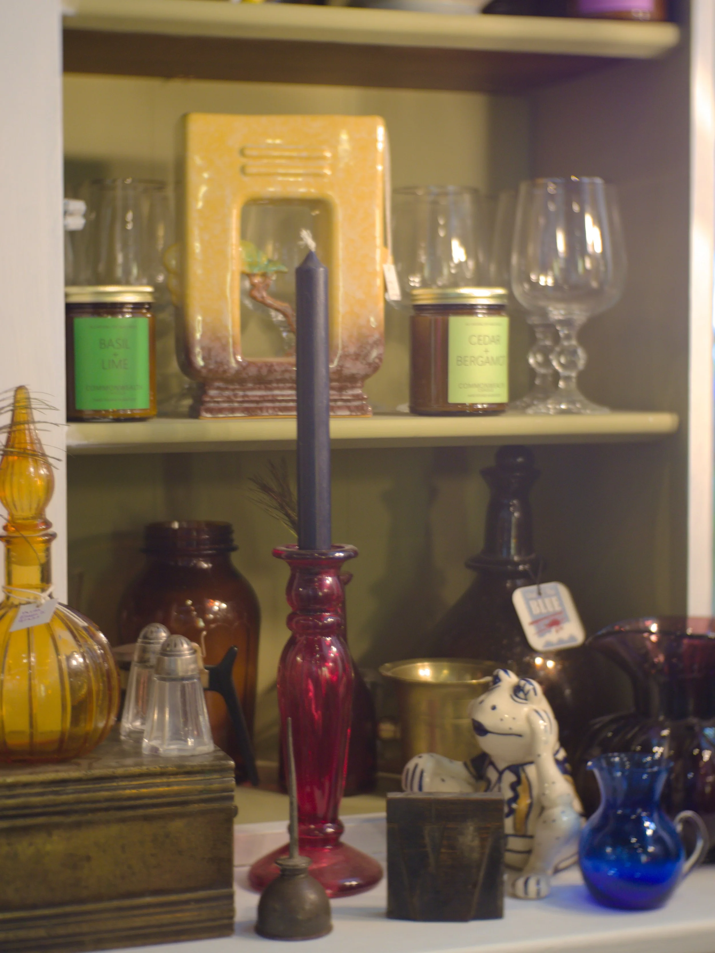 A display of various decorative items including colorful glass vases, ceramic animal figurines, a candle holder, and jars with labels on a shelf.