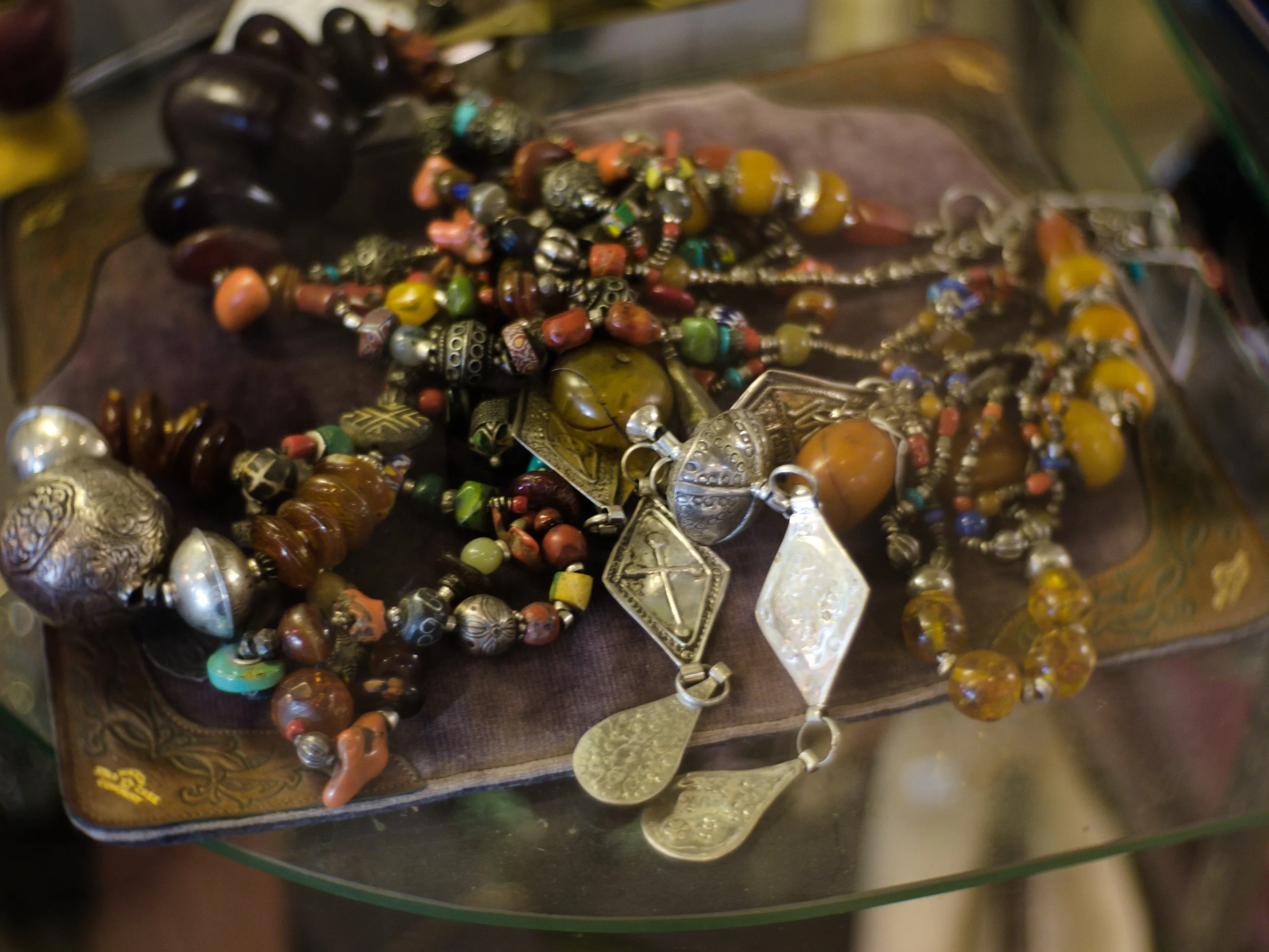 Display of various jewelry pieces including beads, necklaces, and silver ornaments on a dark tray.