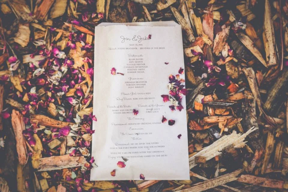 Wedding program on wood chips with flower petals scattered on top.