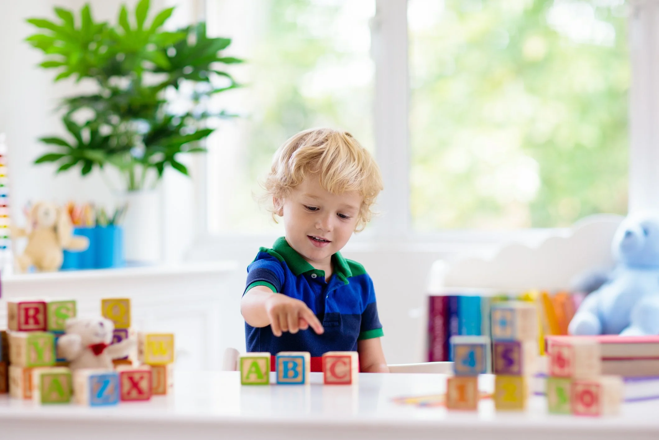 A preschool boy is playing with colorful letter blocks on a table.