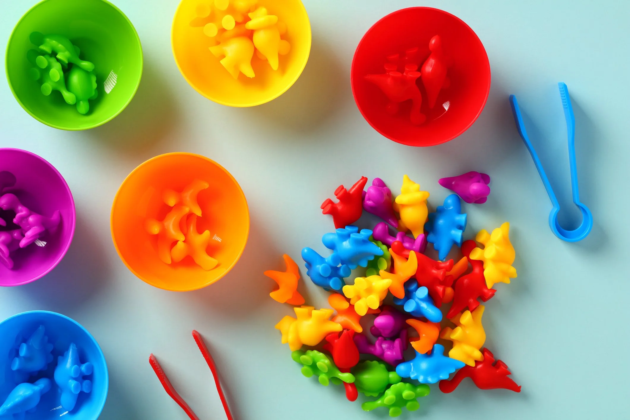 Colorful dinosaur counters are on a table with colorful bowls.