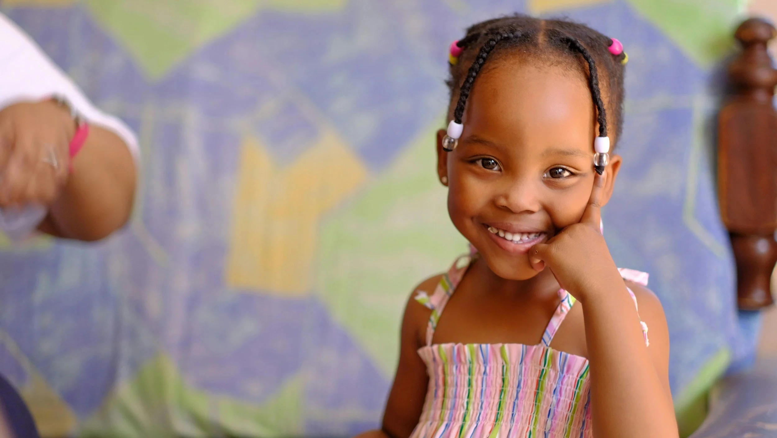 Young girl smiling in front of a blue, green, and yellow board.