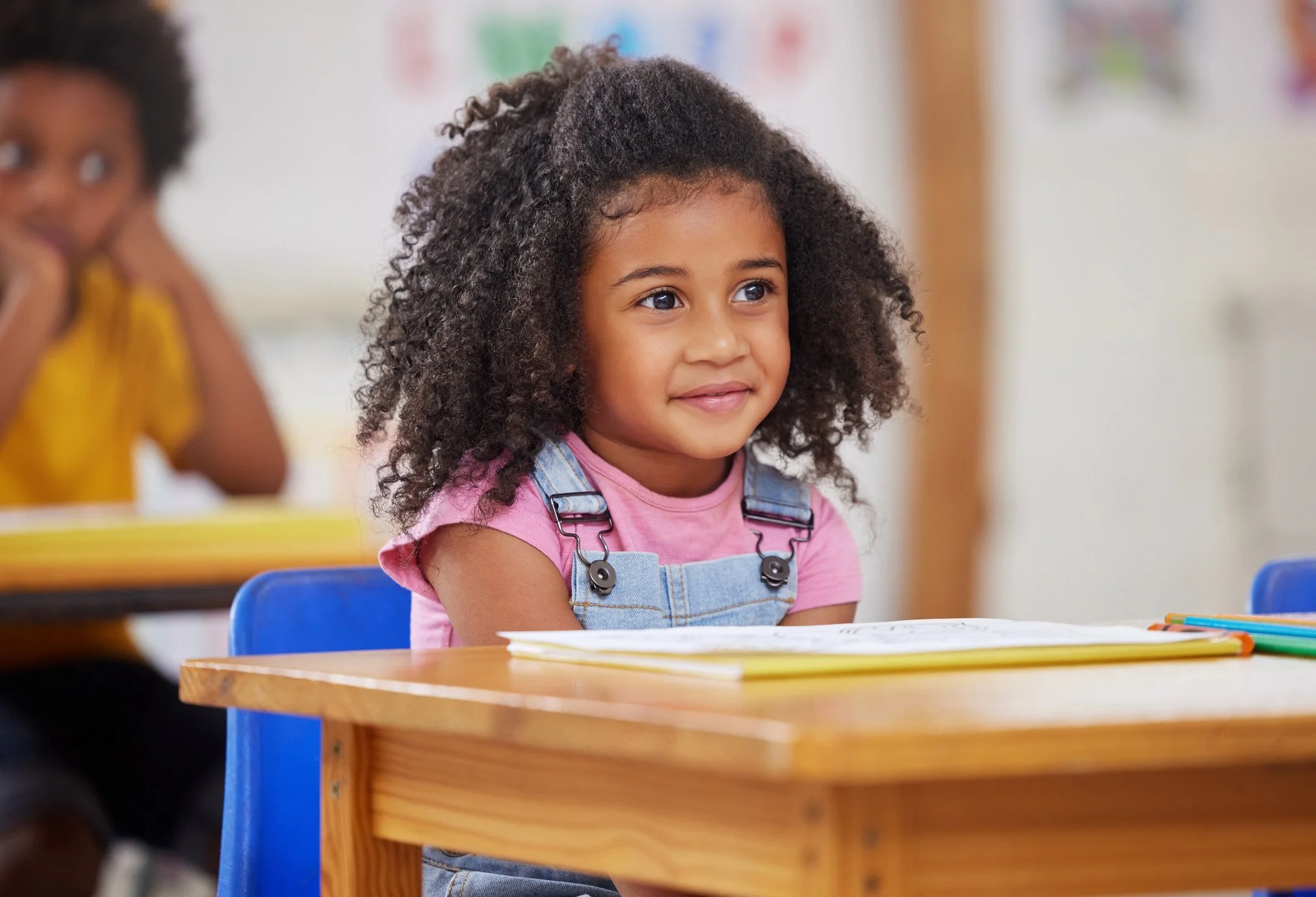 Young girl smiling while sitting at a desk in a classroom.