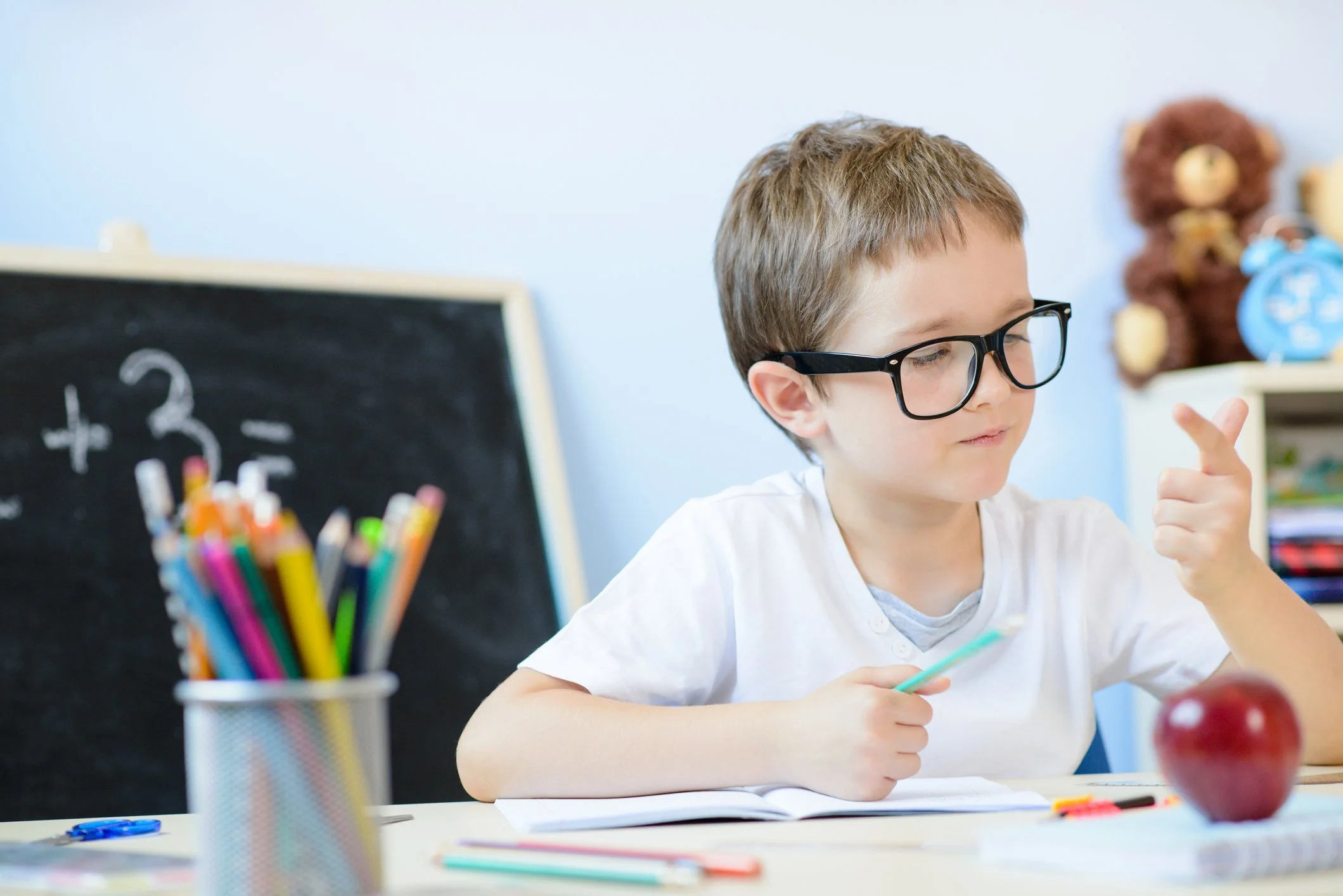 A young boy is sitting at a desk with school supplies.