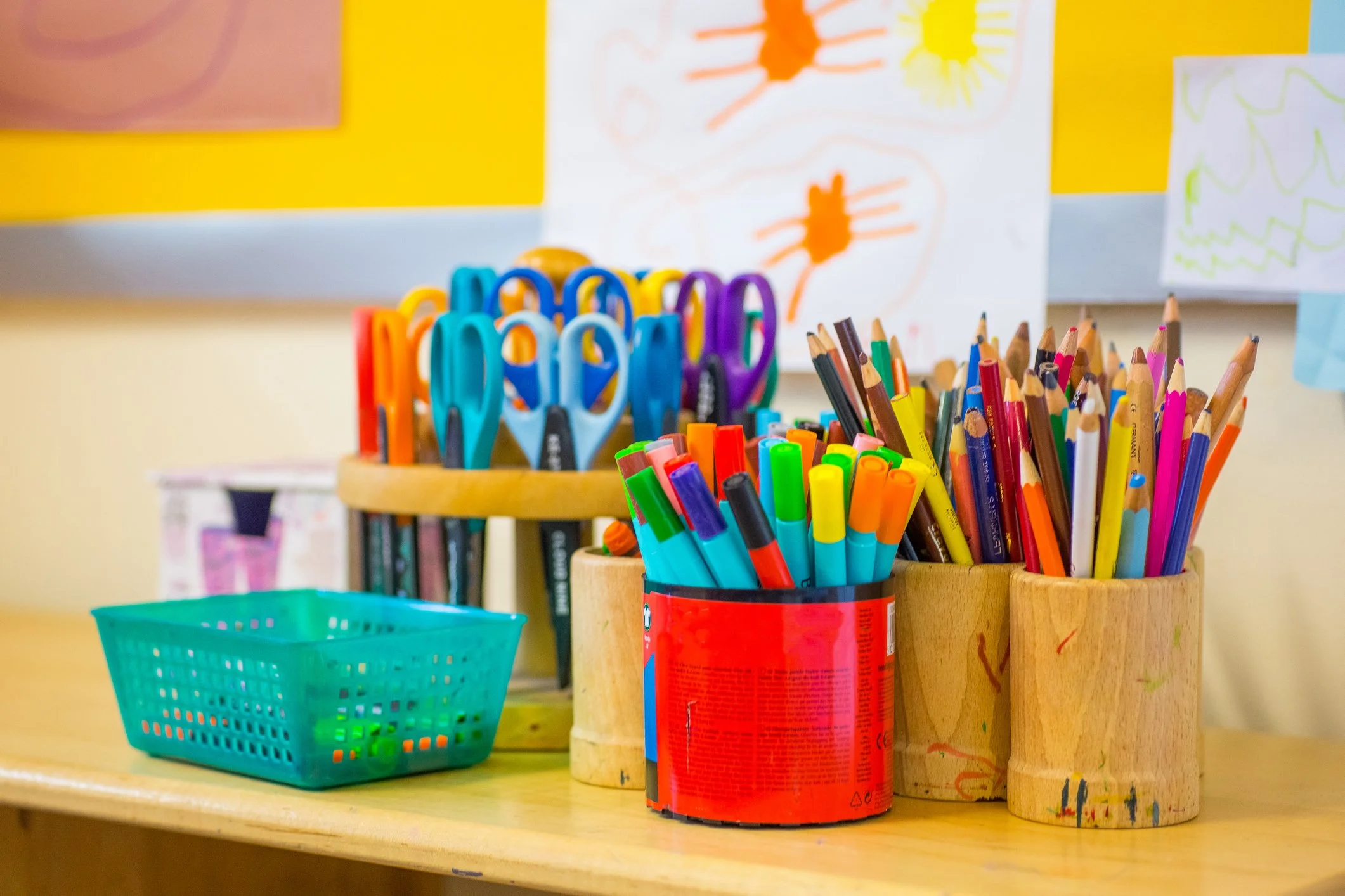 Colorful craft supplies including scissors, markers, and colored pencils are organized in containers on a shelf.