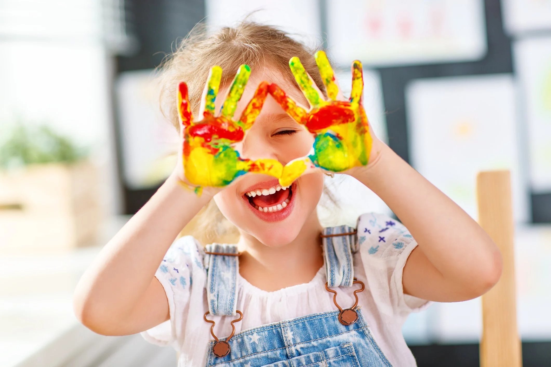 A little girl is smiling and holding up her hands colorful painted hands.