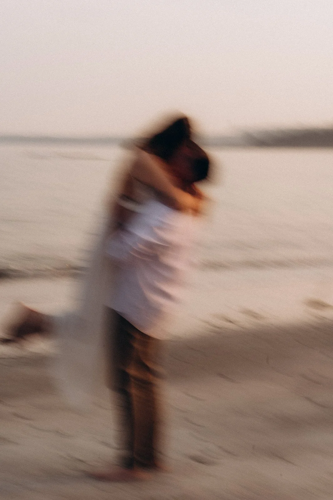 A blurry photo of a woman on the beach during sunset, embracing a child.