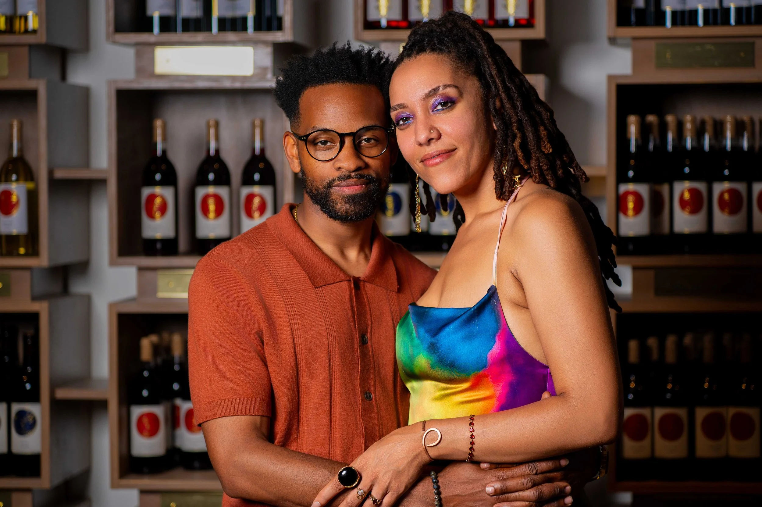 A man and woman standing close together, smiling, in front of shelves of wine bottles at Waters Edge Winery in Norfolk.