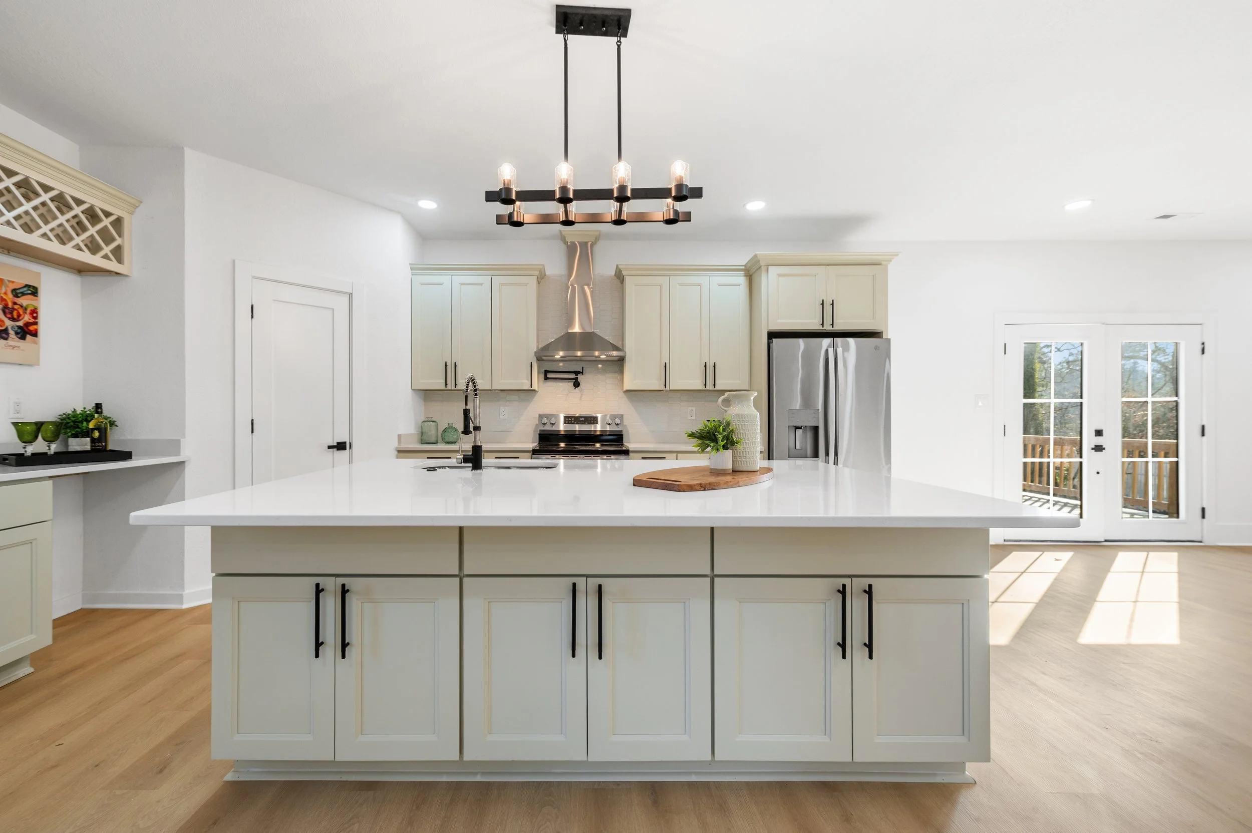 Modern kitchen with white cabinets, stainless steel appliances, and a large island with a wood cutting board and plant.