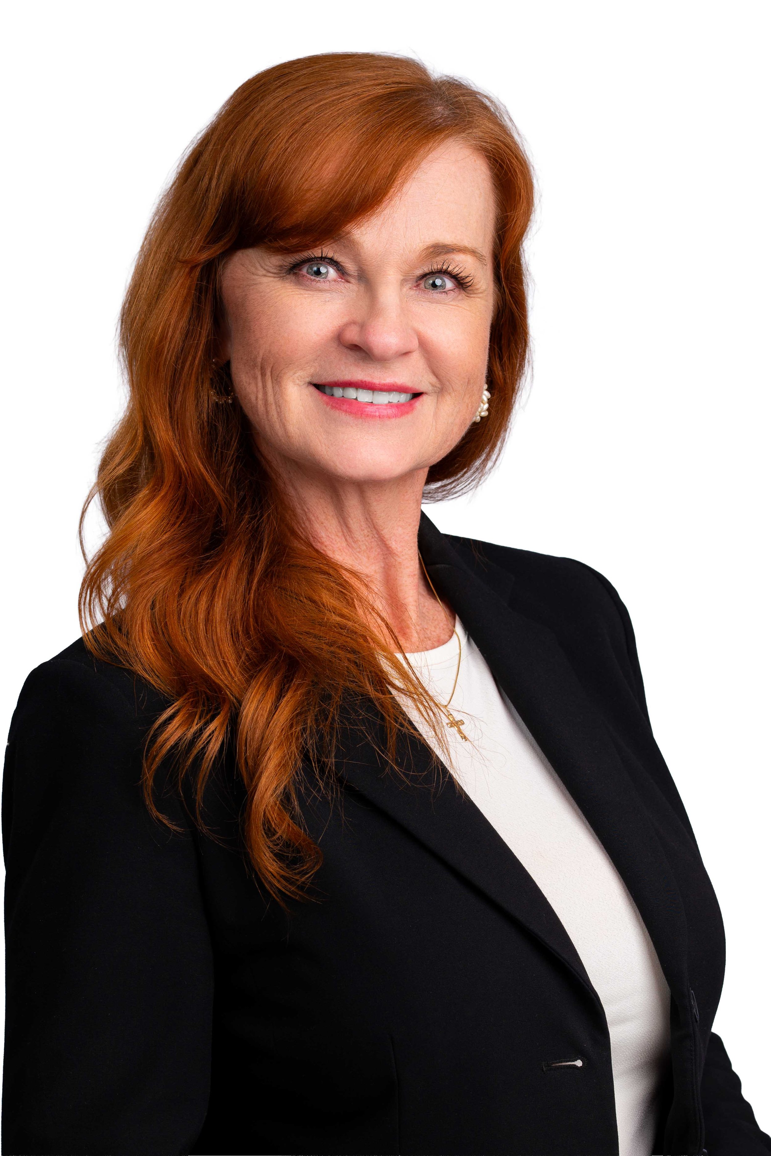 Professional headshot of a smiling woman with long red hair, wearing a black blazer and earrings, against a white background.