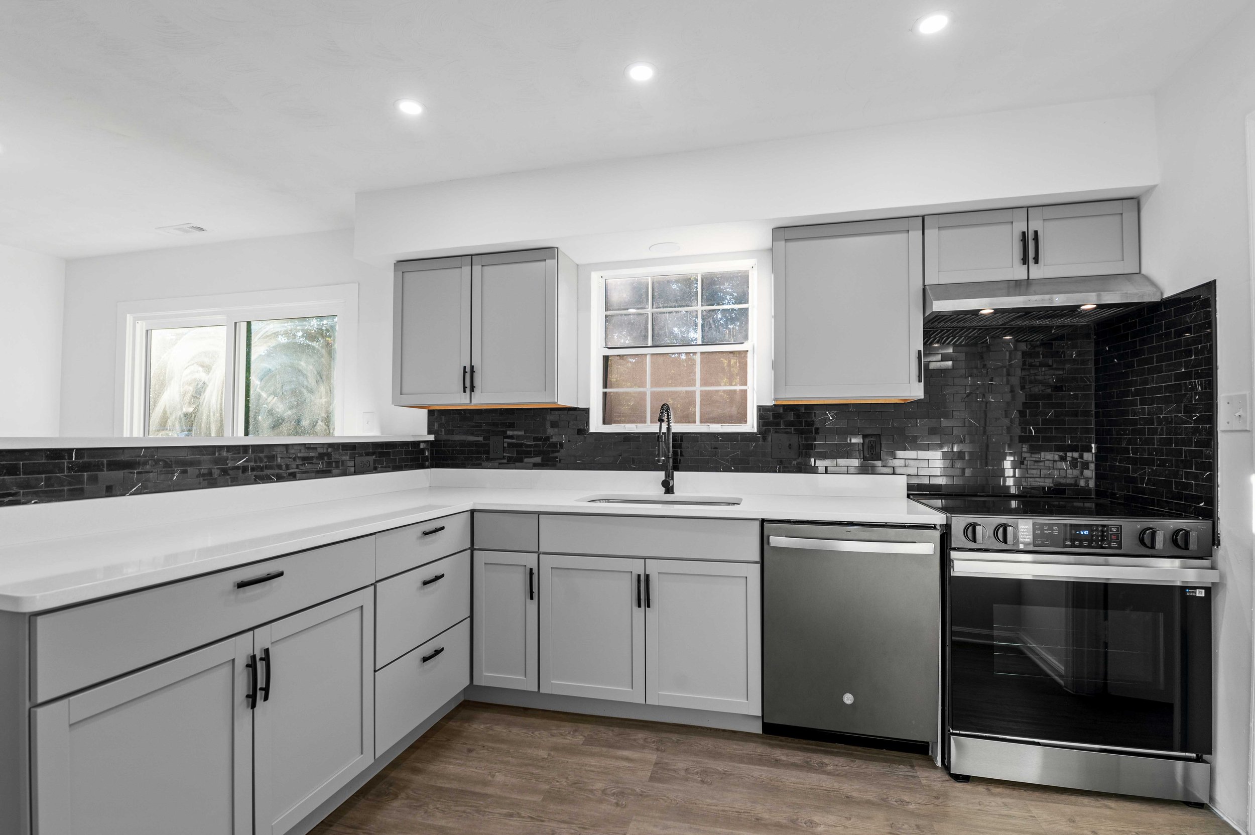 Modern kitchen with white cabinets, black backsplash, stainless steel appliances, and wood flooring.
