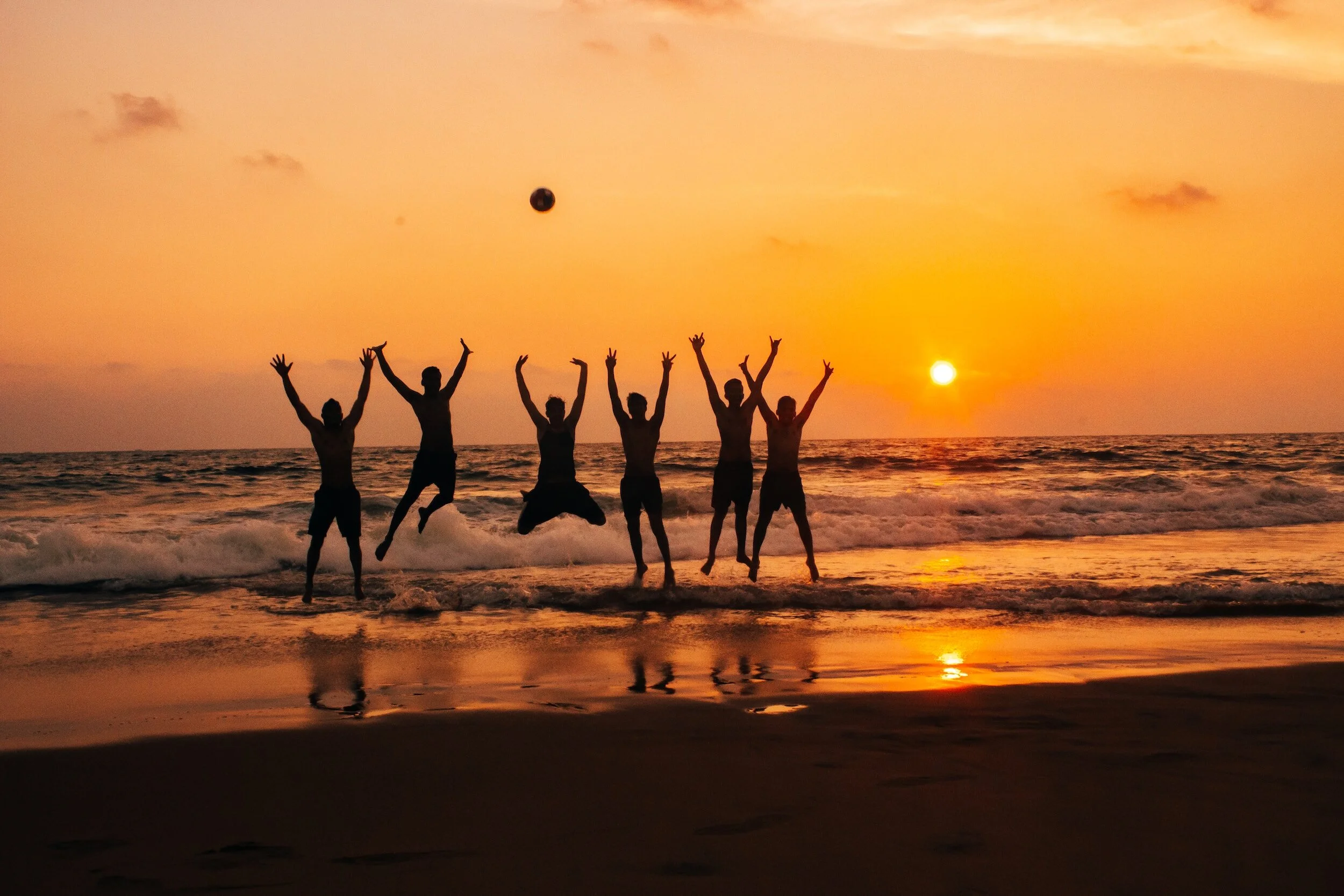 friends on the beach jumping in the water at sunset
