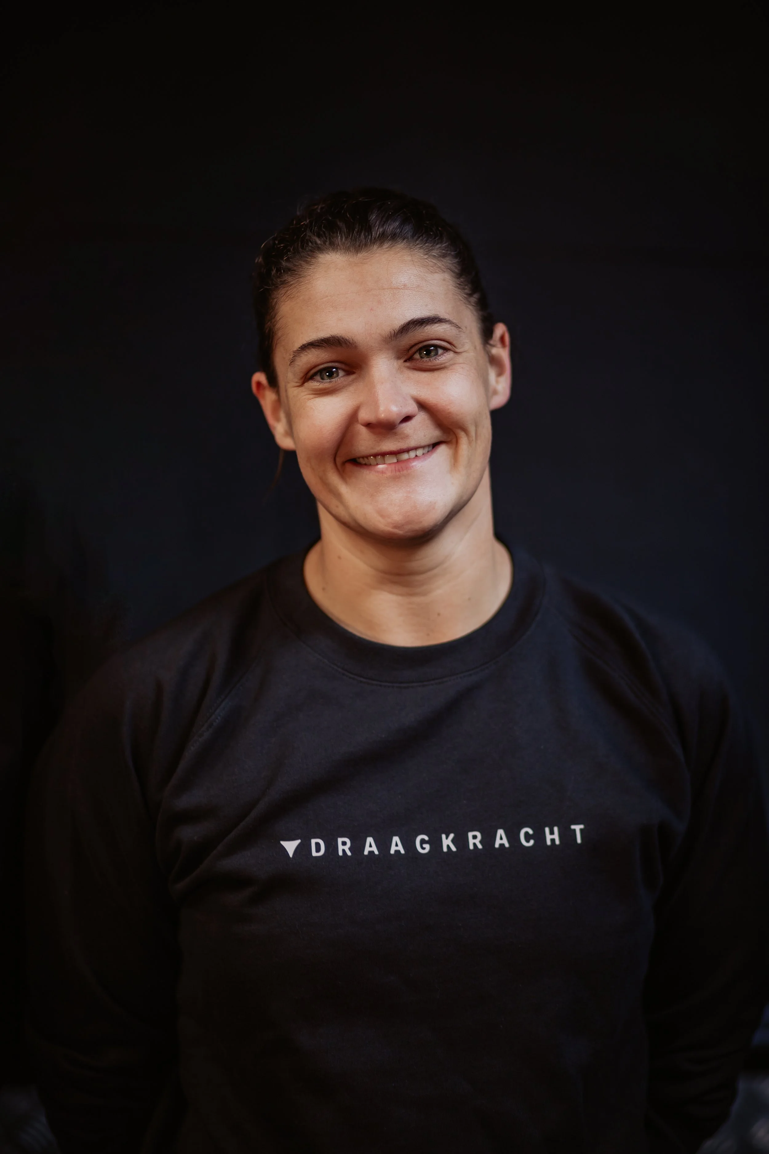 Young woman with a smile, holding a thick rope in a gym or fitness facility.
