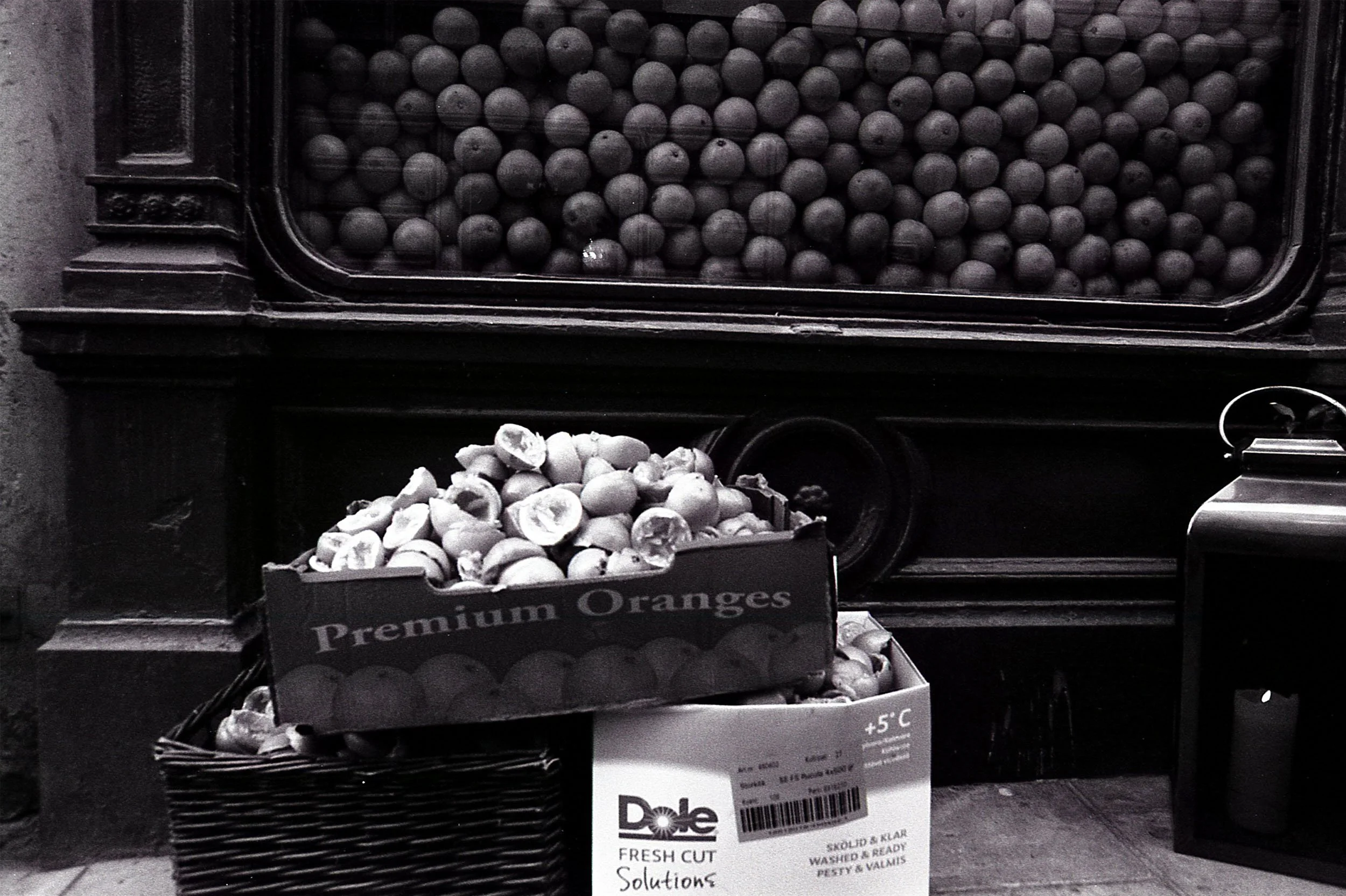 A vending machine with black and gray balls, with a basket of peeled oranges and a sign indicating fresh-cut solutions for sale.