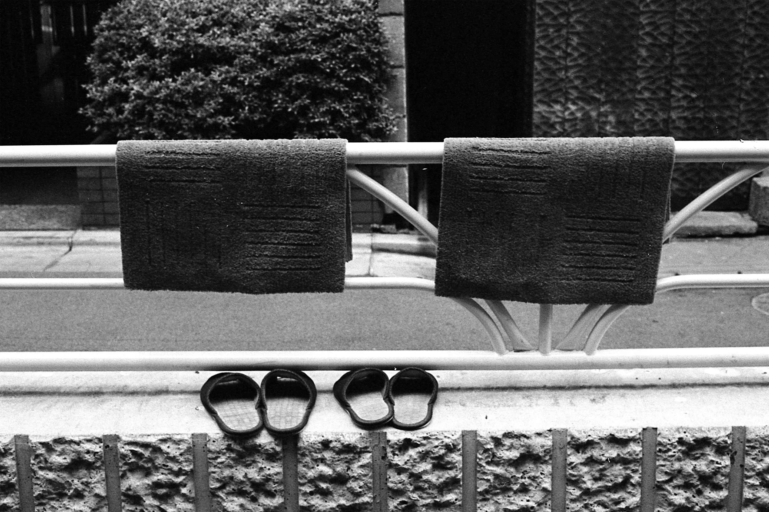 A black and white photo of tennis rackets leaning against a brick wall, with stacked tennis balls underneath.