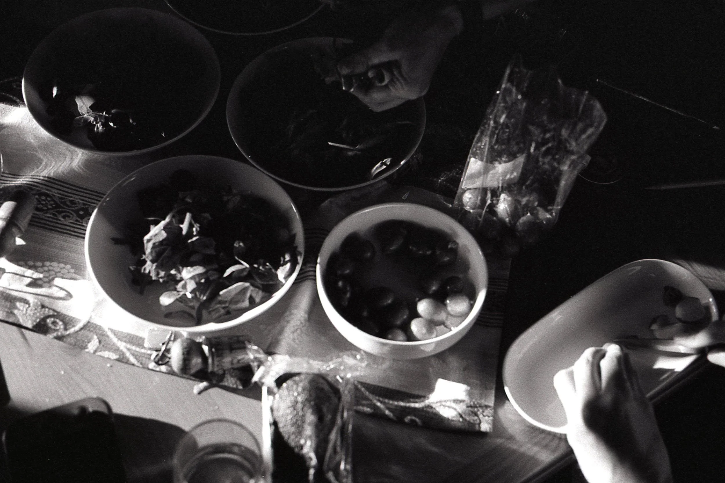 A collection of bowls containing various small items, possibly food or objects, on a patterned tablecloth, with some plastic bags nearby.