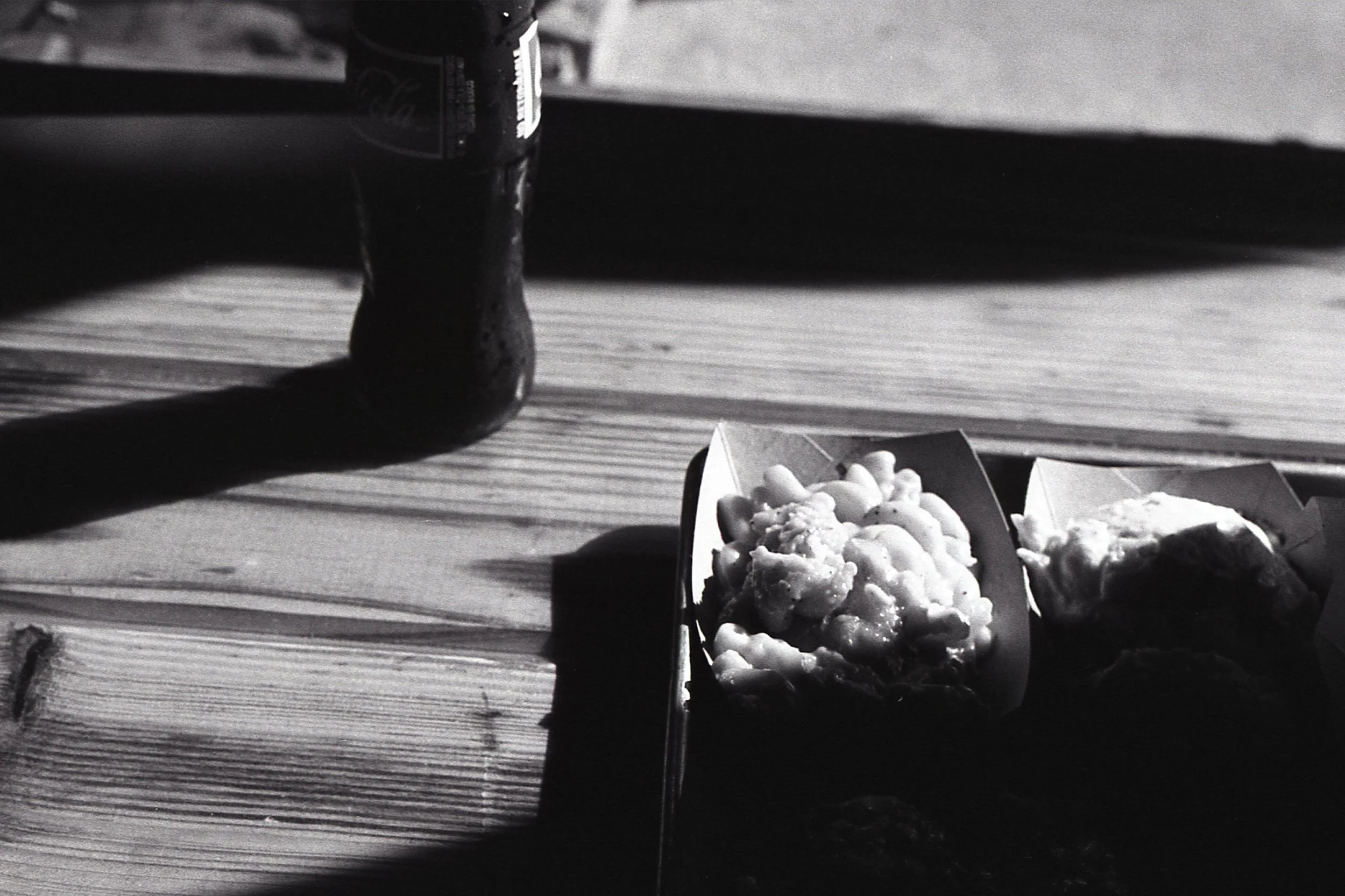 Black and white photo of two pizza slices in cardboard boxes on a wooden table, with a soda can in the background.