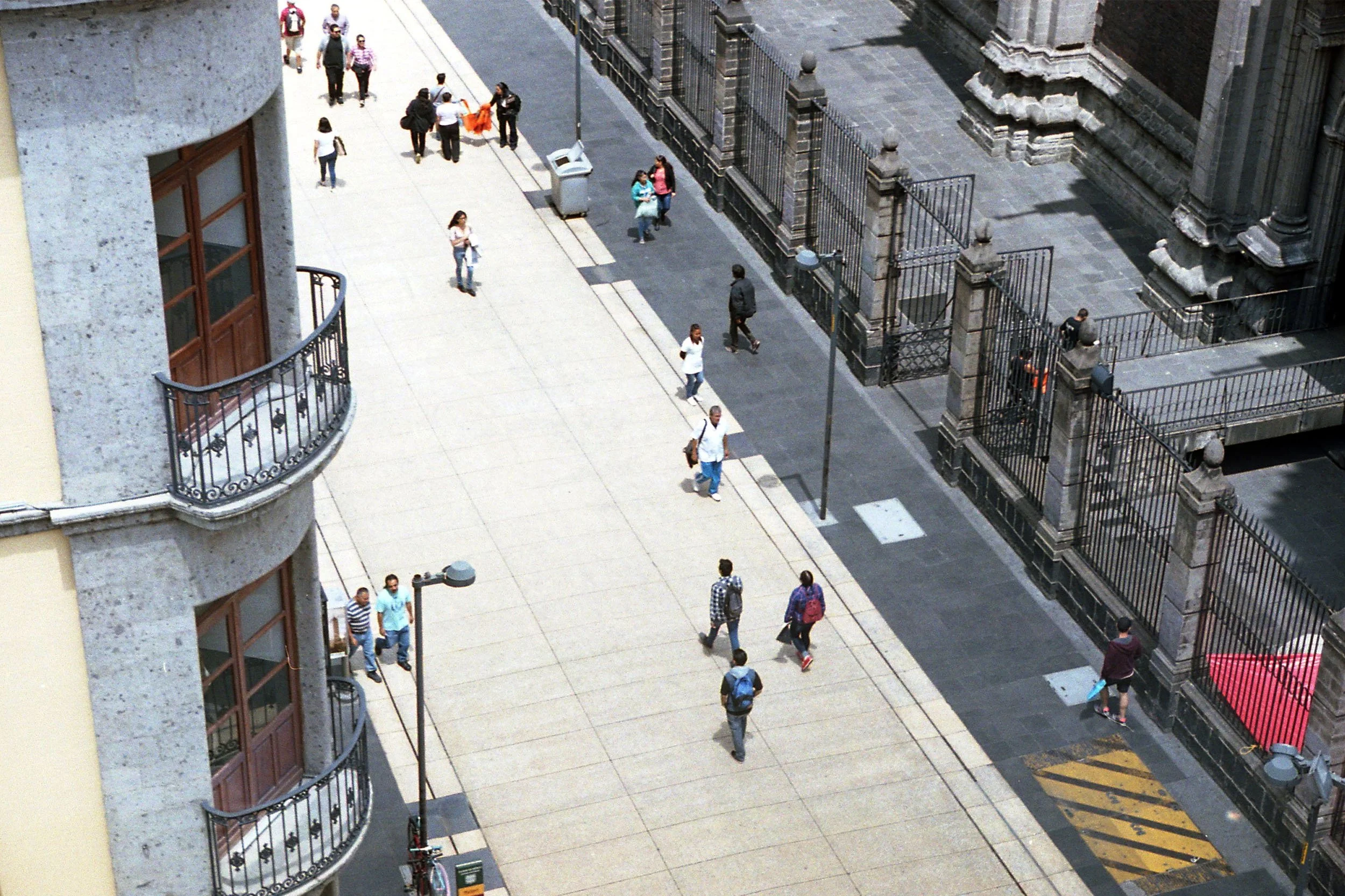 Color photo of shot from a roof looking down onto people walking along the sidewalk