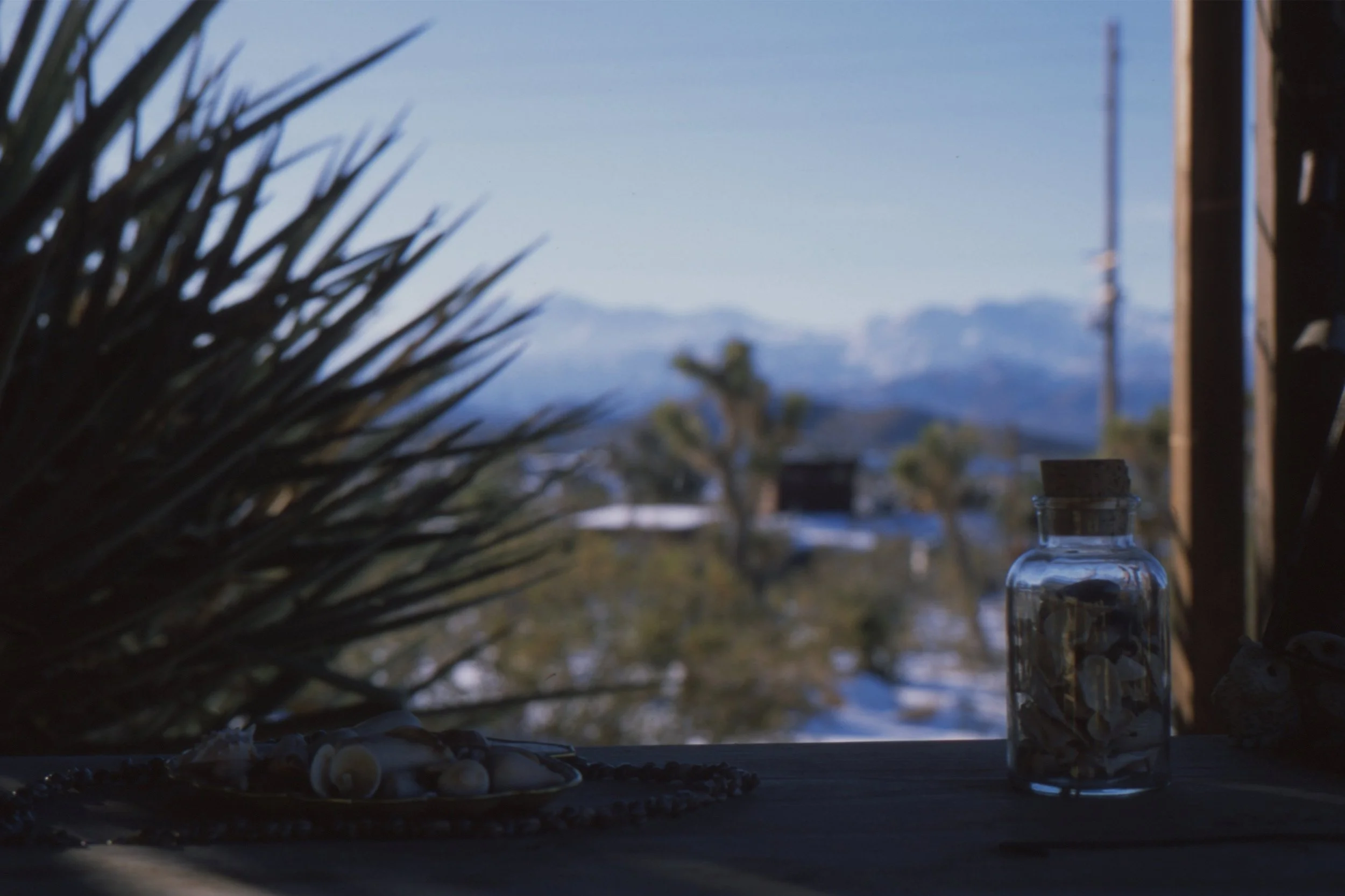 Blurred view of a window with a bottle on the windowsill, overlooking a landscape with mountains in the distance.