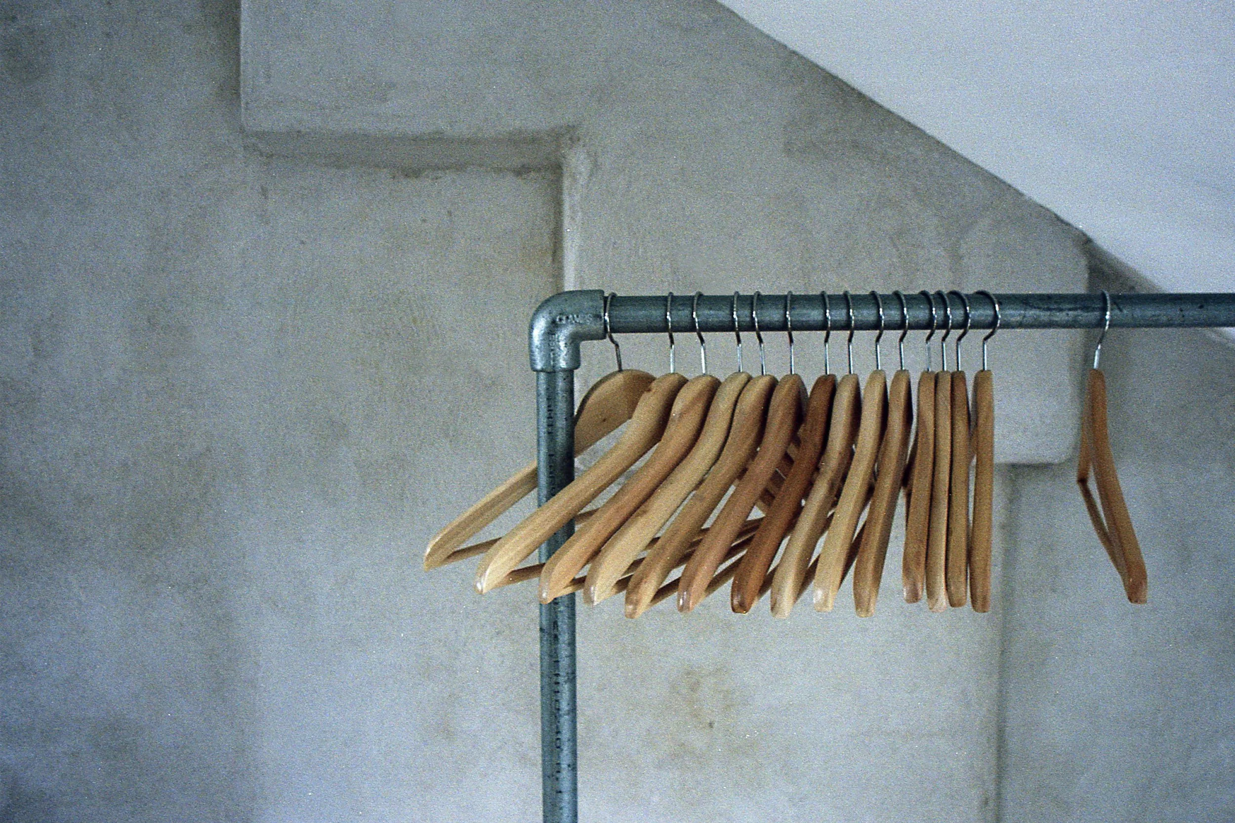 A clothing rack with wooden hangers against a gray wall.