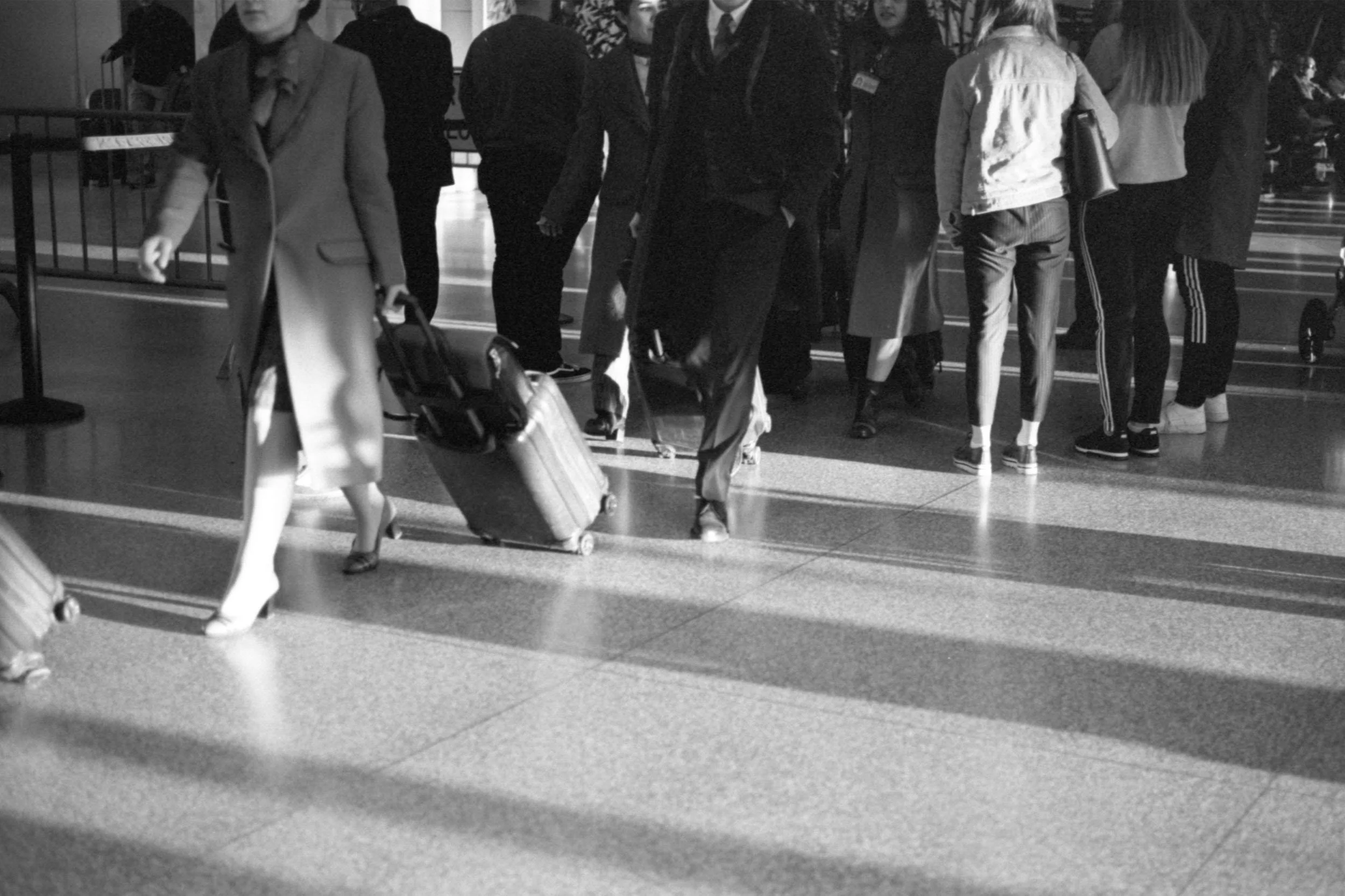 Black and white photo of people's legs as they walk with suitcases at airport