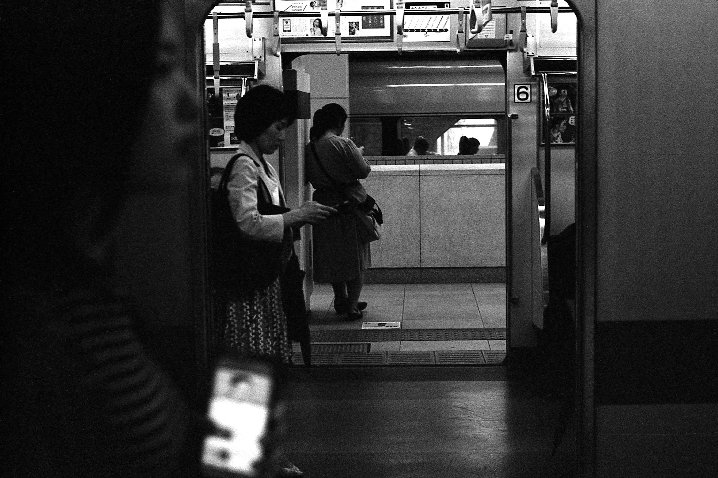 Black and white image looking from subway onto platform with women on their phones