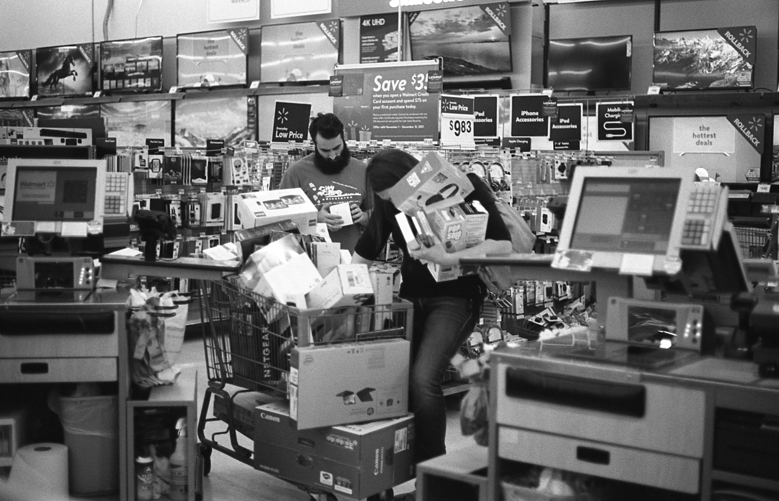 Black and white photo of two people loading up a full shopping cart at walmart