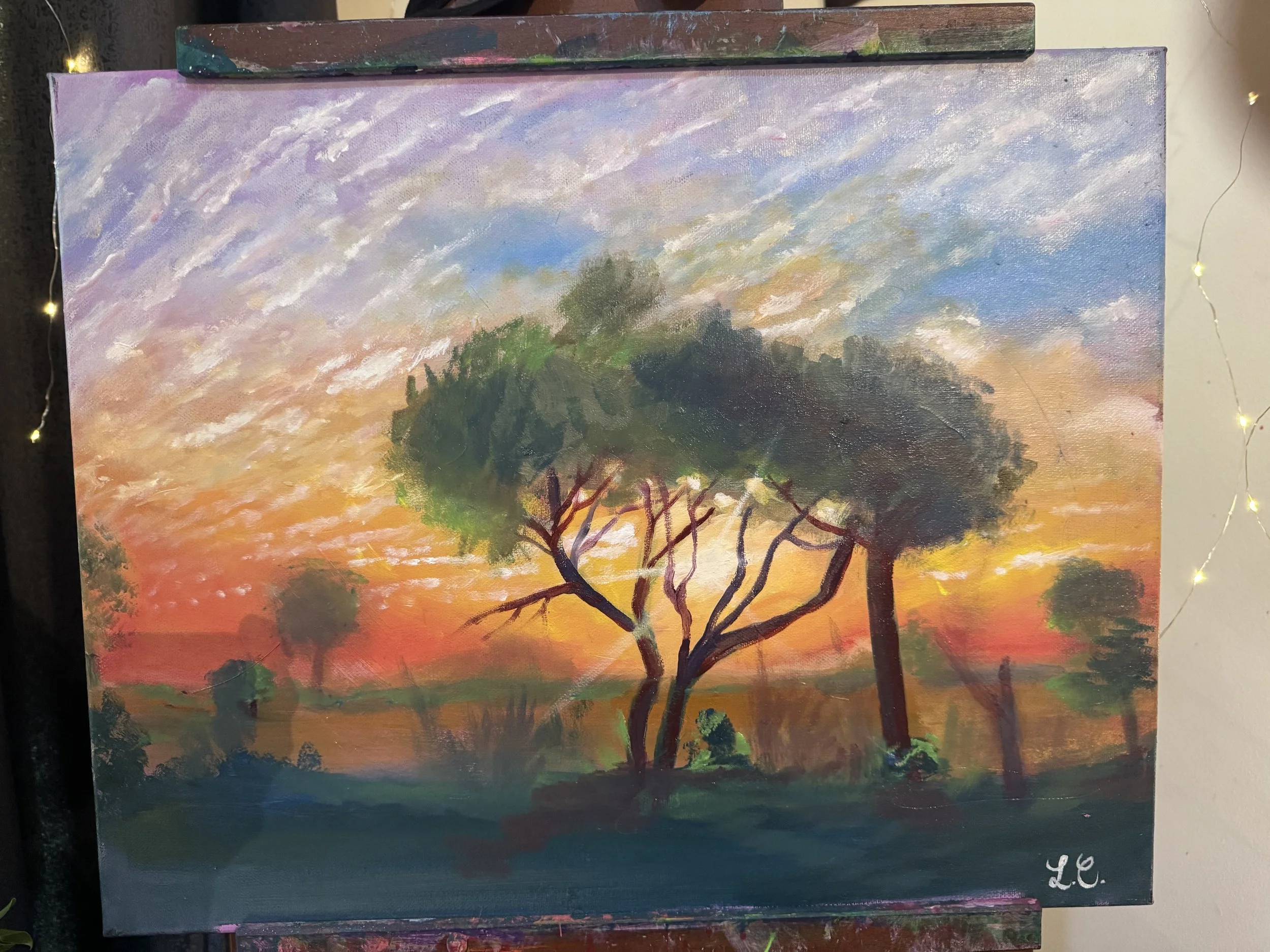 A landscape painting of a sunset with colorful skies, showing clouds, trees, and a distant horizon.