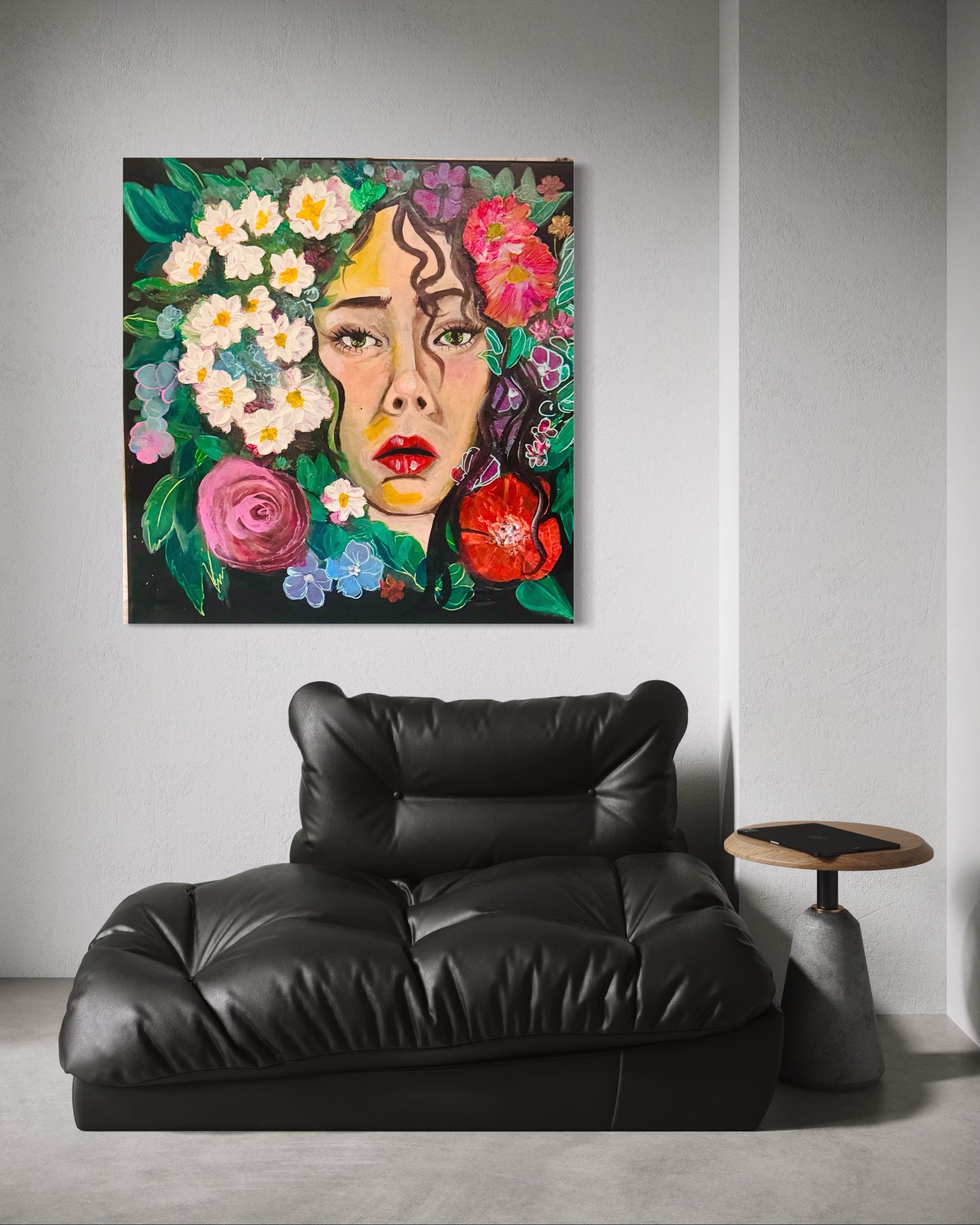 A modern living room with a black leather sofa, a wooden side table with a tablet, and a colorful portrait of a woman with flowers on the wall.
