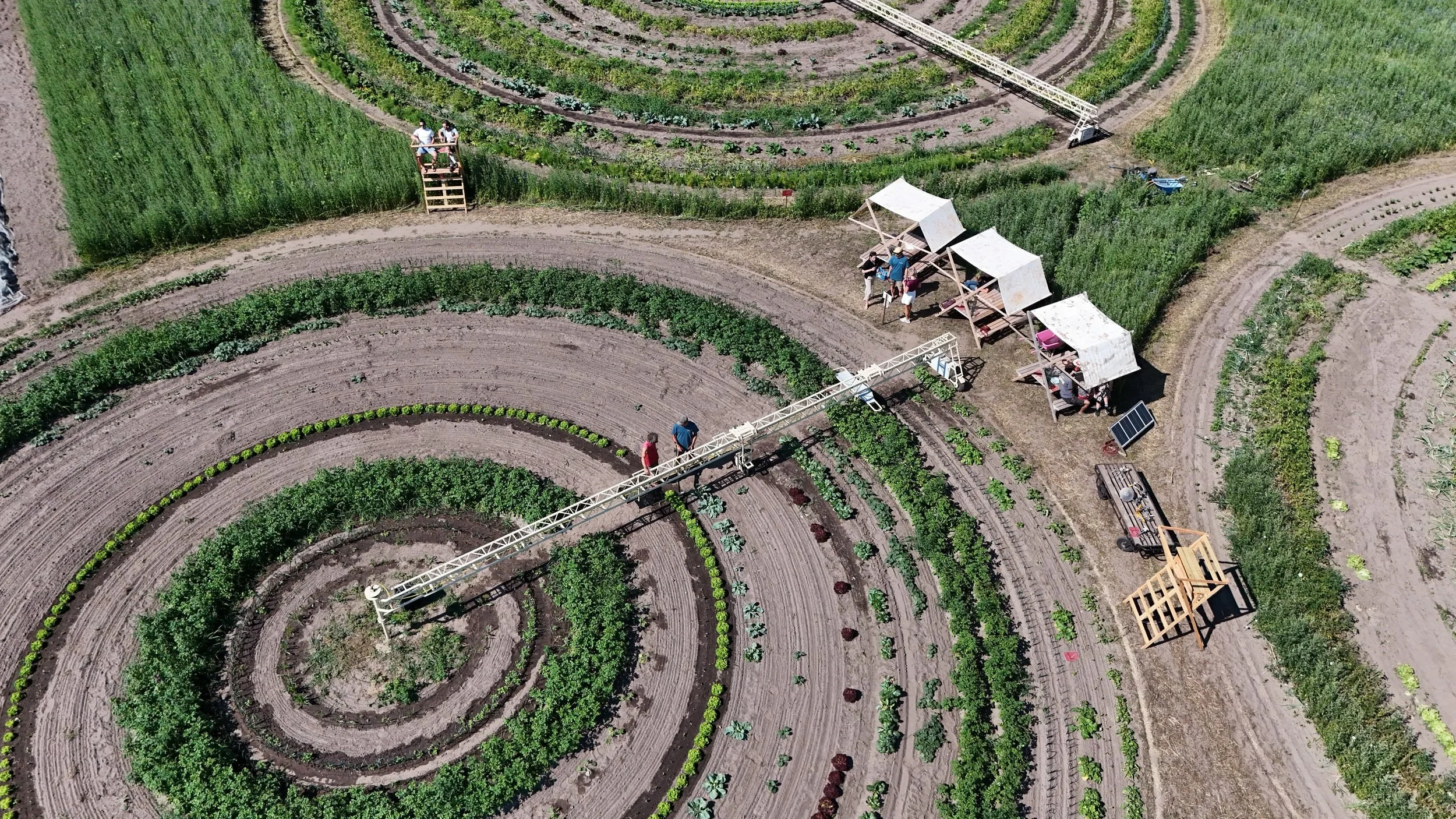 Luchtfoto van een nieuwe vorm van land verbouwen in circkels en mensen die werken met of staan onder schaduwrijke overkappingen.