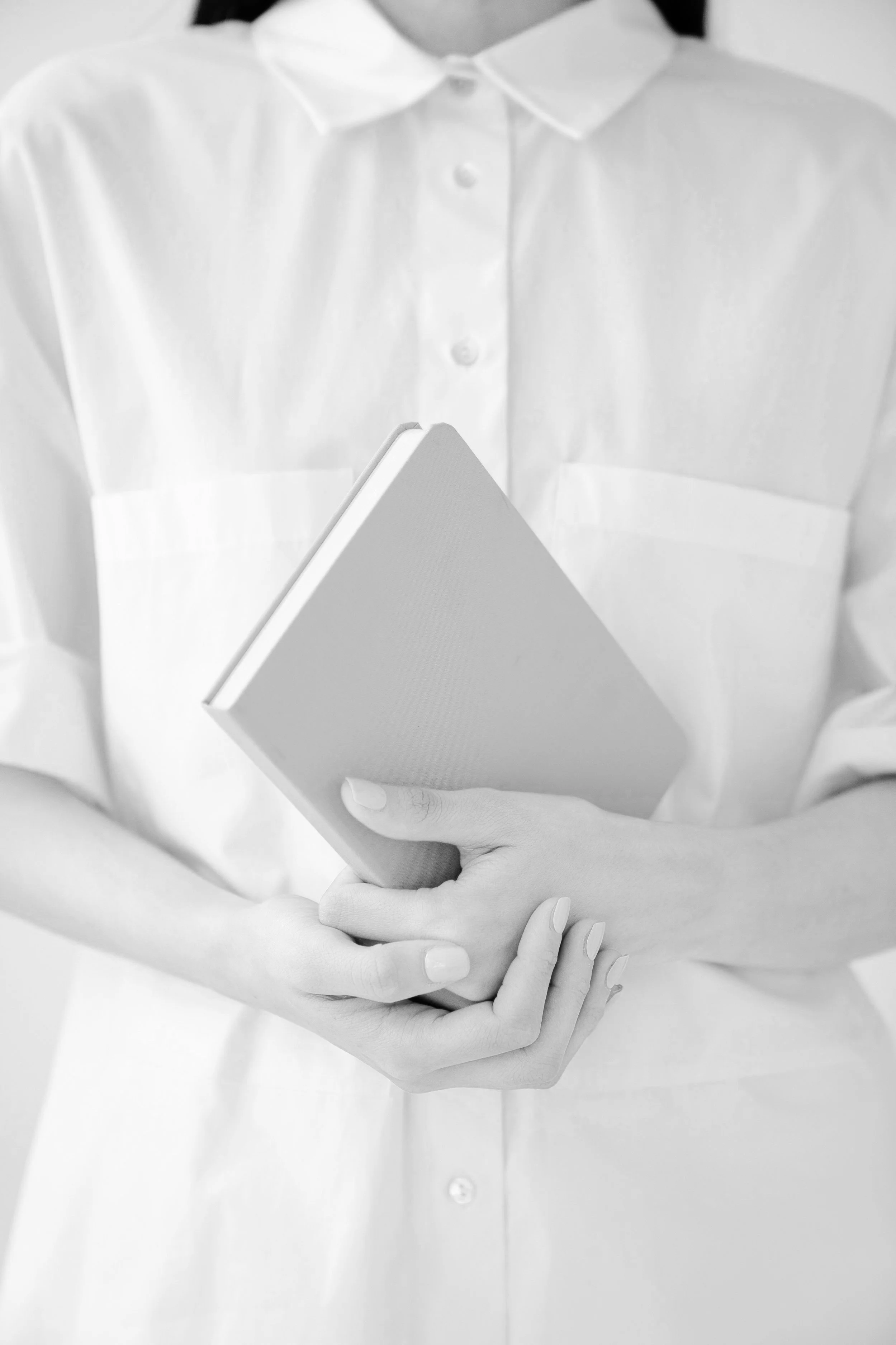 Person wearing a white shirt holding a closed book or notebook with both hands.