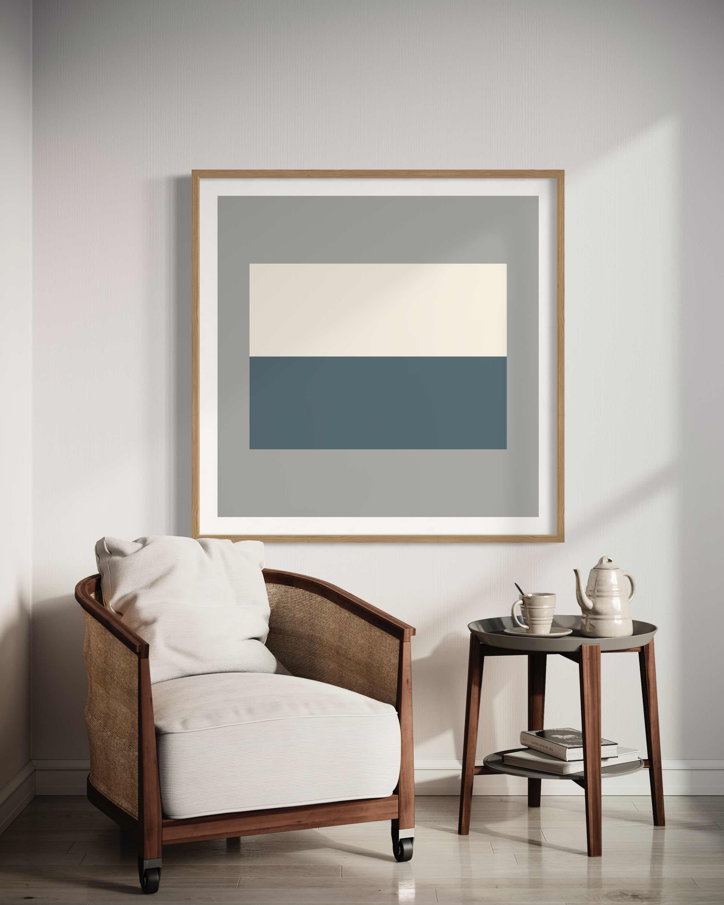 A cozy corner in a living room with a white cushioned armchair with wooden frame, white pillow, a black side table with white teapot, mug, and books, and a framed abstract art piece with geometric shapes hanging on the wall.