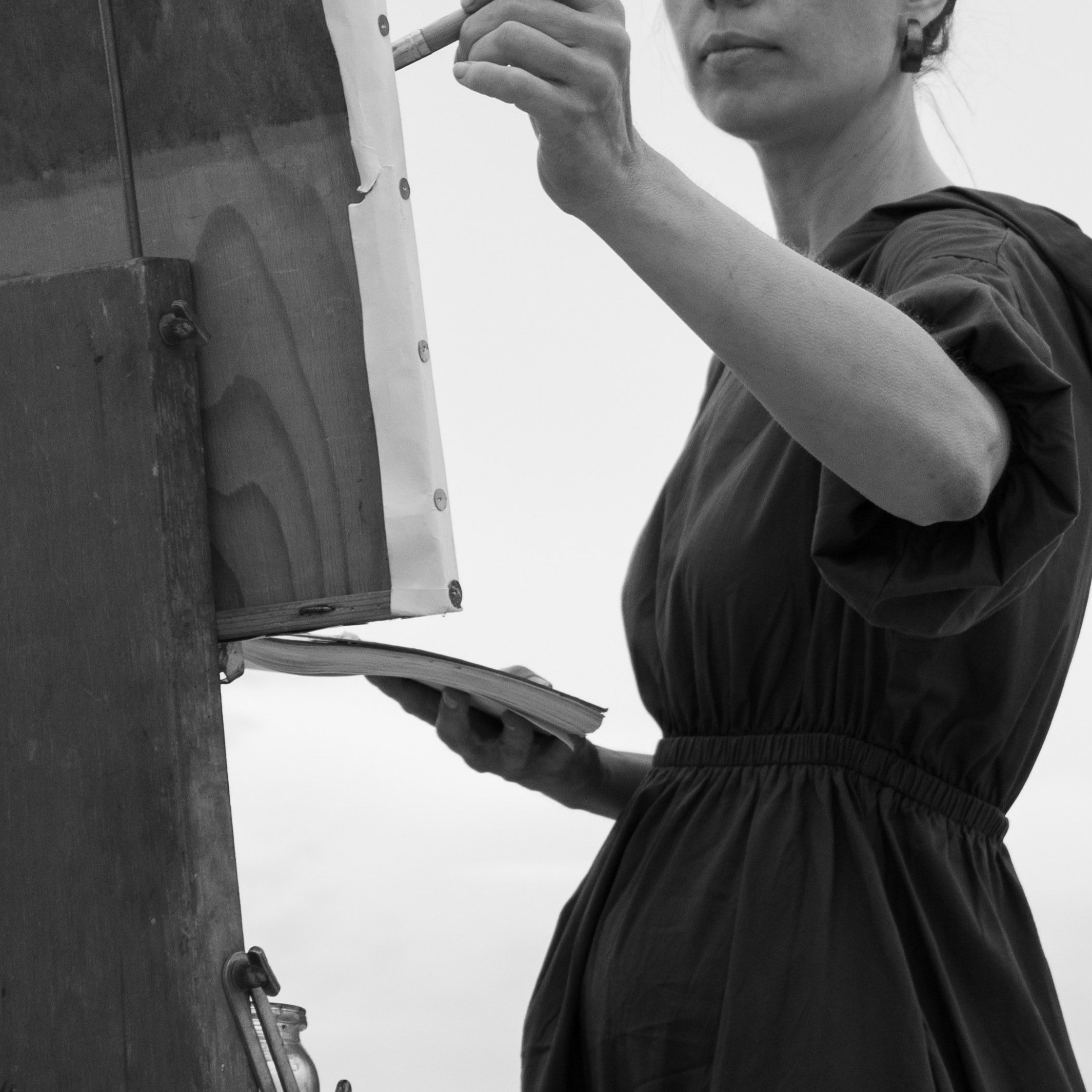 A person drawing or writing on a vertical surface, possibly a chalkboard or whiteboard, with a marker or chalk in their right hand. The person is wearing a dark short-sleeved shirt.